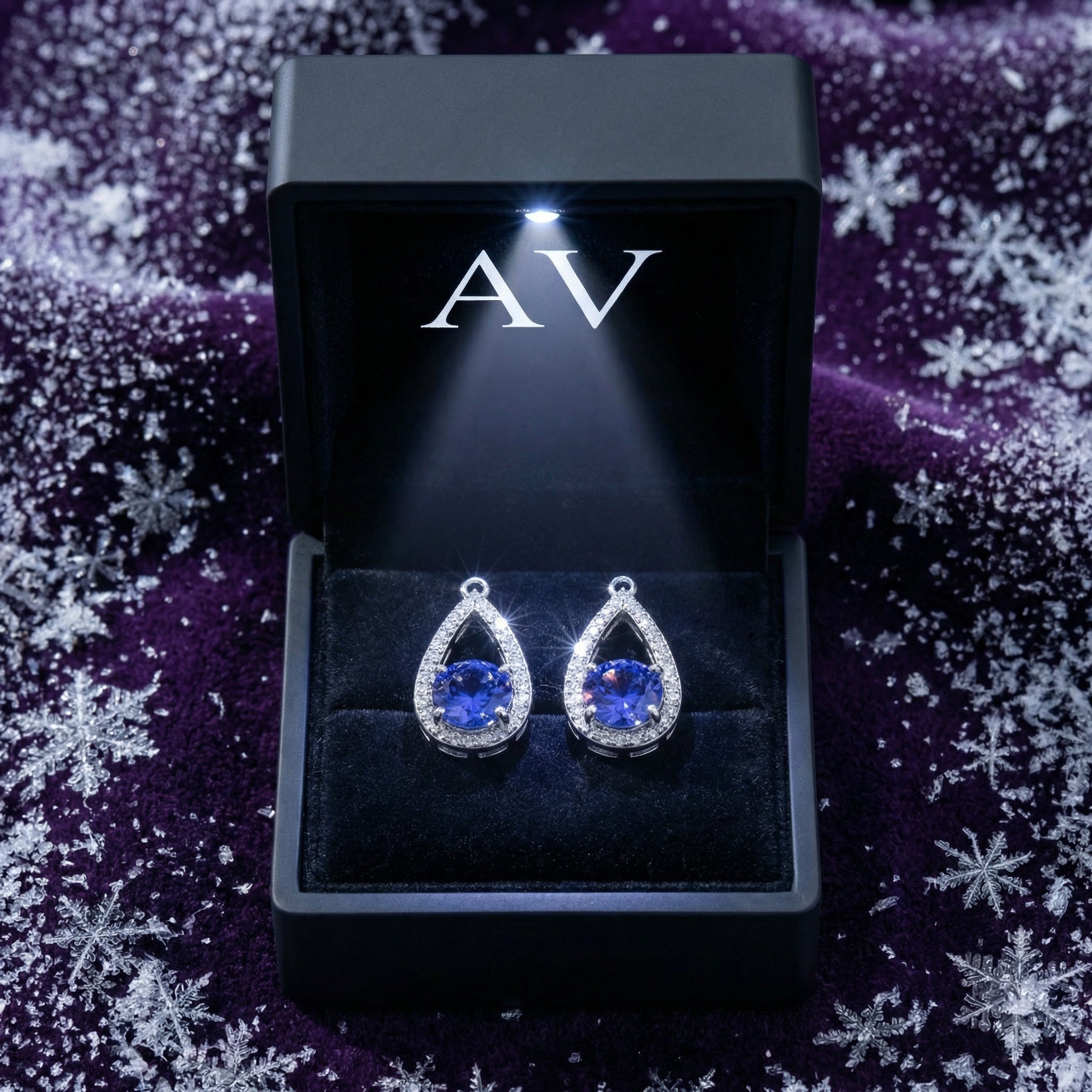 Sterling silver teardrop earrings with blue simulated tanzanite in a lighted black gift box on purple velvet.