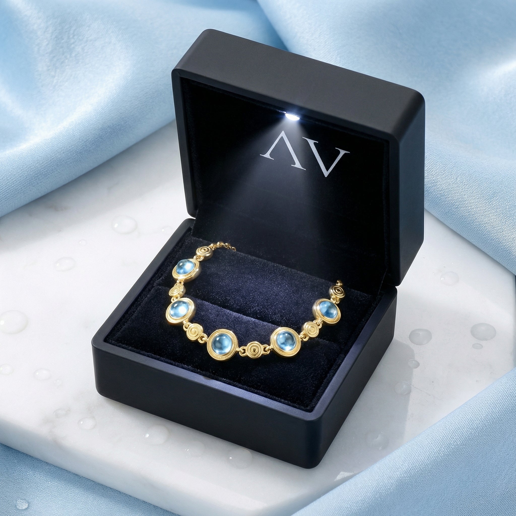 The Marisol gold vermeil bracelet with blue simulated aquamarine stones in a black lighted jewelry gift box.