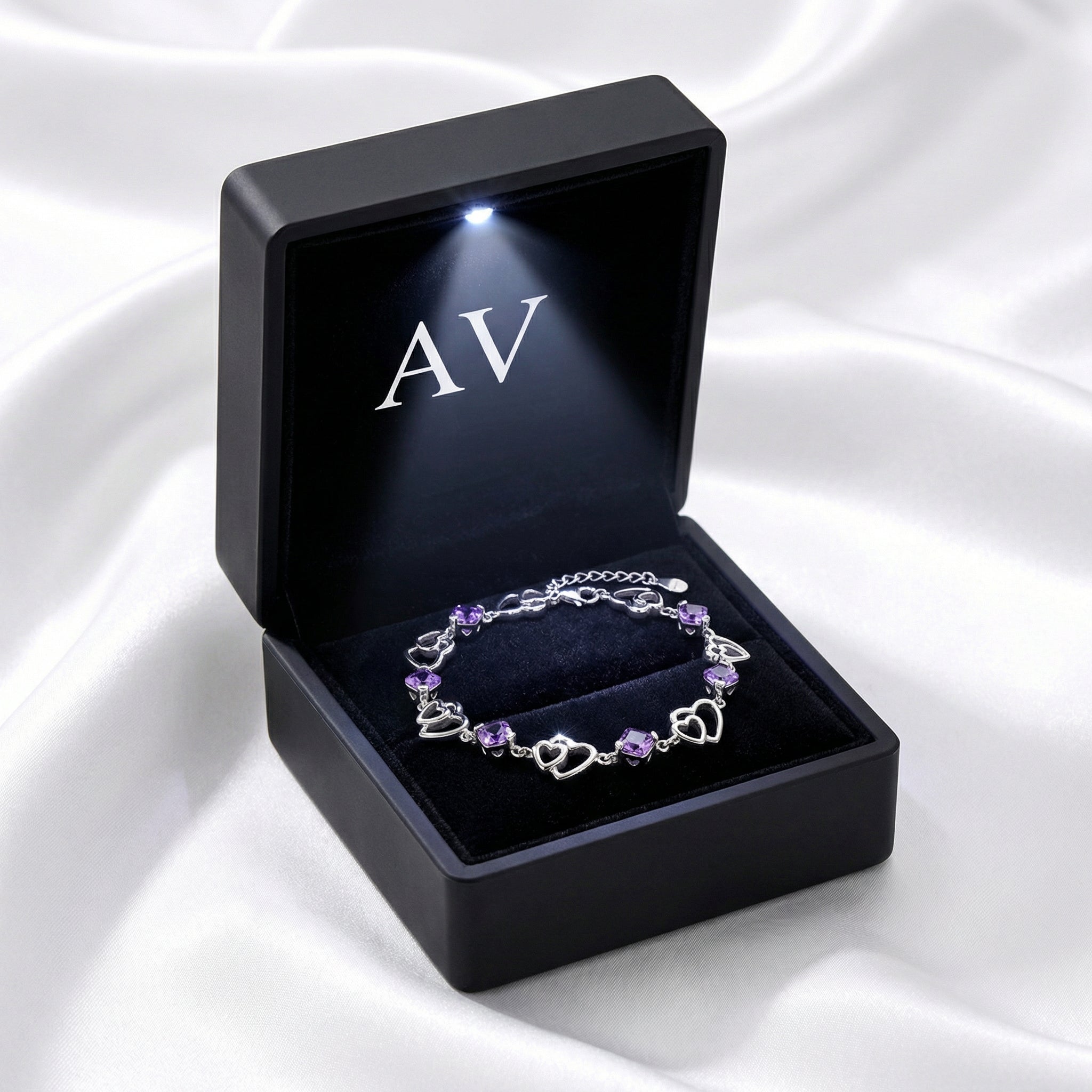 Sterling silver heart link bracelet with purple stones inside a black LED-lighted jewelry gift box.