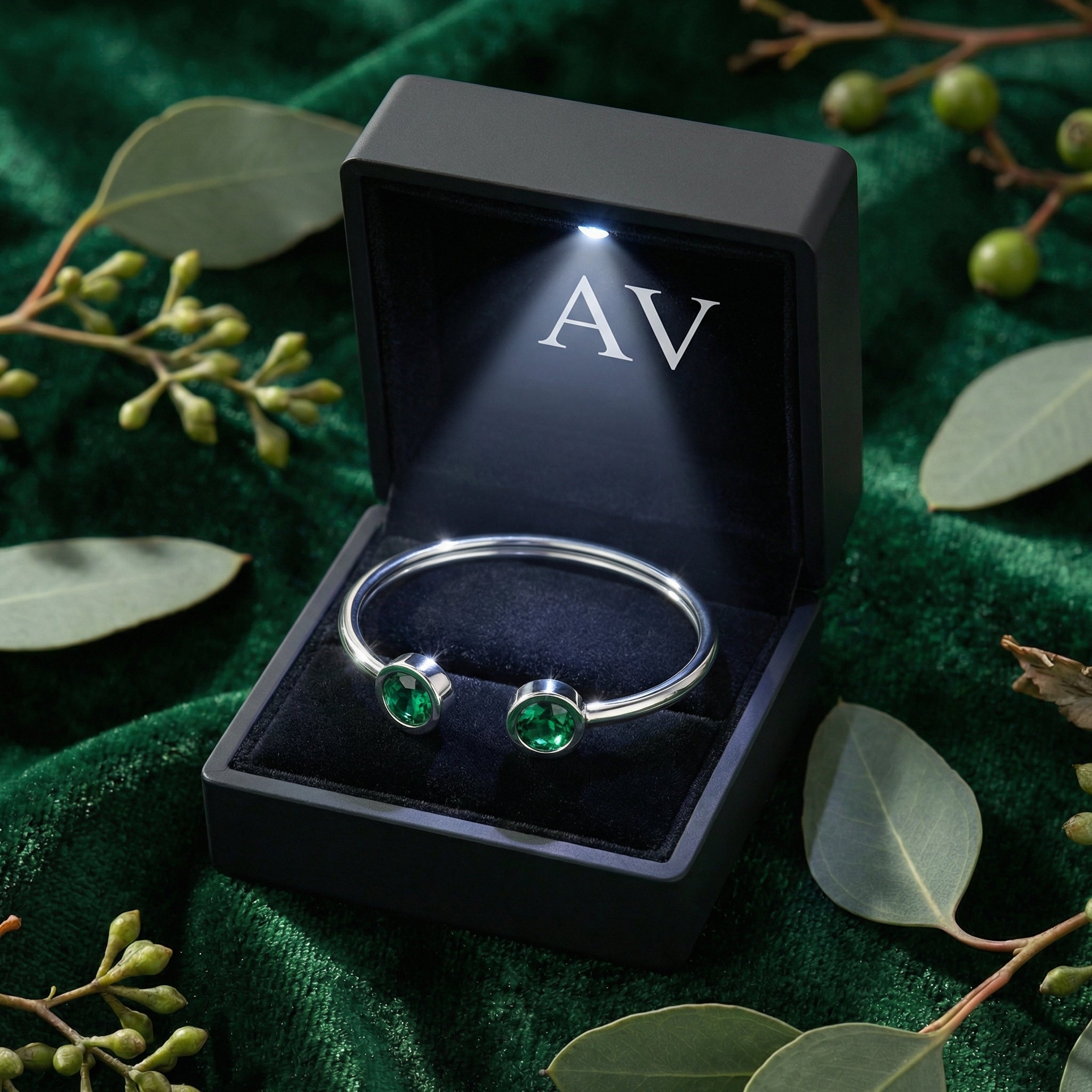 Silver stainless steel bypass cuff bracelet with round simulated emeralds in a black LED-lit jewelry gift box.