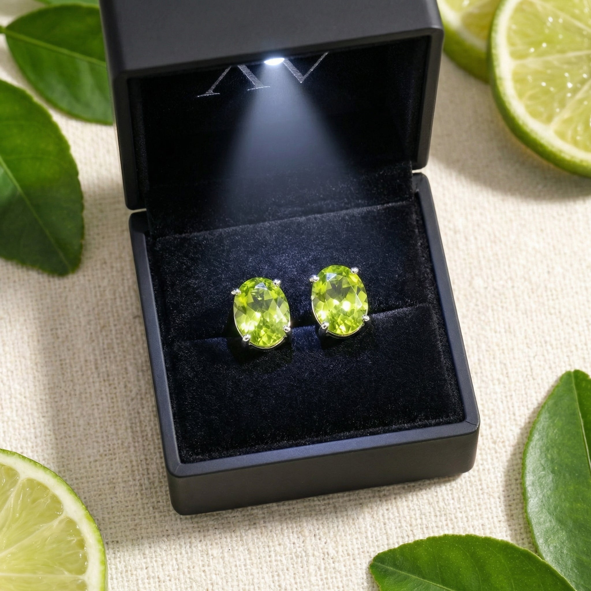 Oval-cut simulated peridot stud earrings in silver settings inside a black LED-lighted box with lime accents.