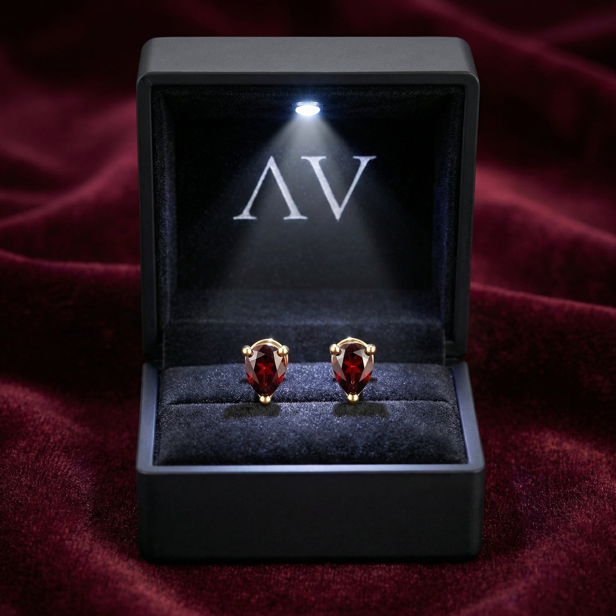 Pear cut simulated garnet stud earrings in 18K gold vermeil inside a lighted black AV jewelry gift box.