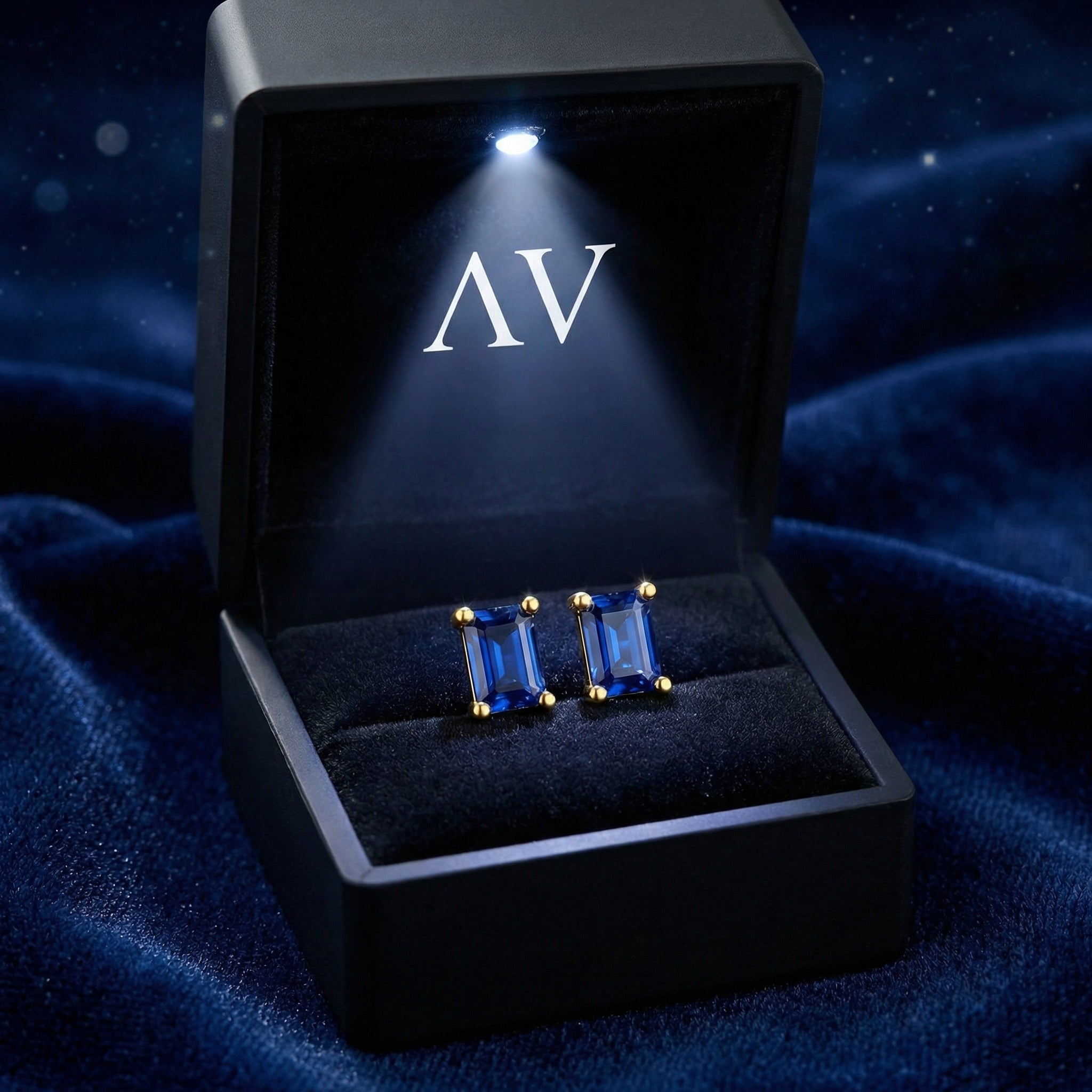 Baguette-cut blue simulated sapphire stud earrings in 18K gold vermeil in a lighted black jewelry box.