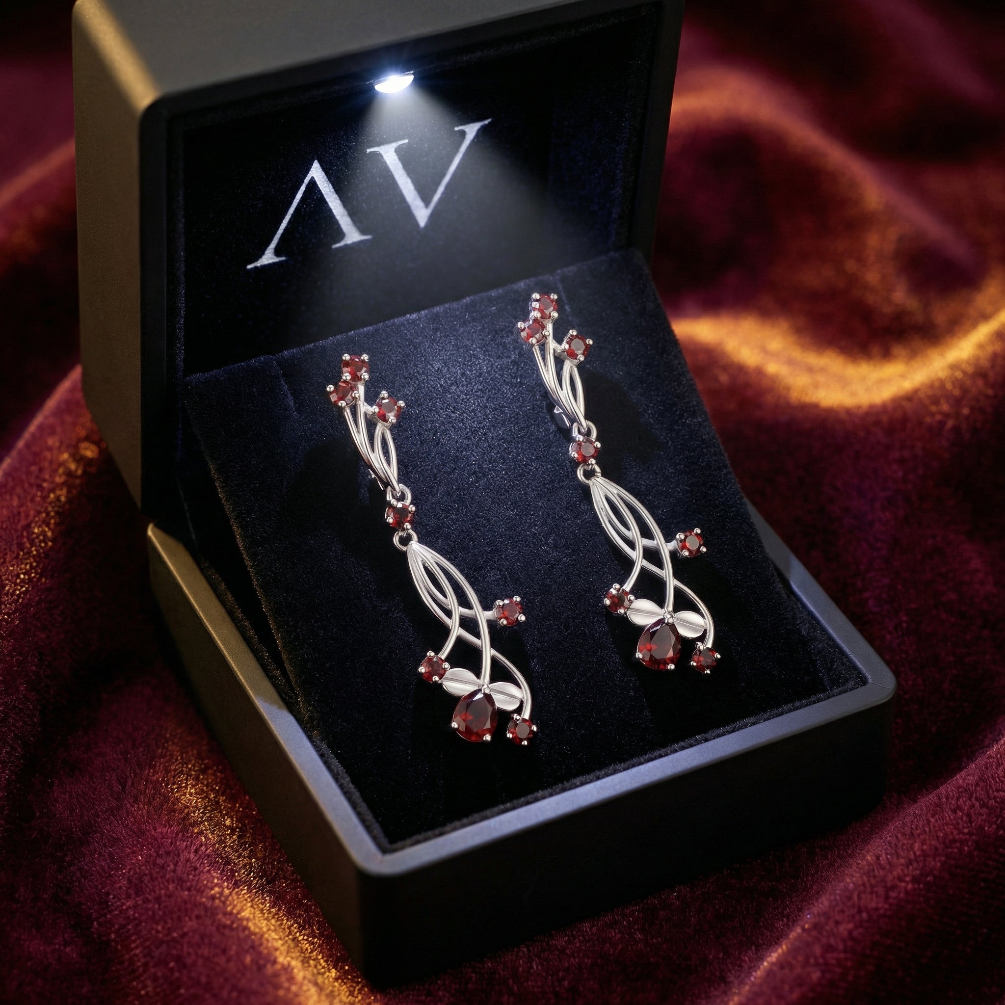The Kalina red garnet drop earrings presented in a black LED-lit gift box on velvet.