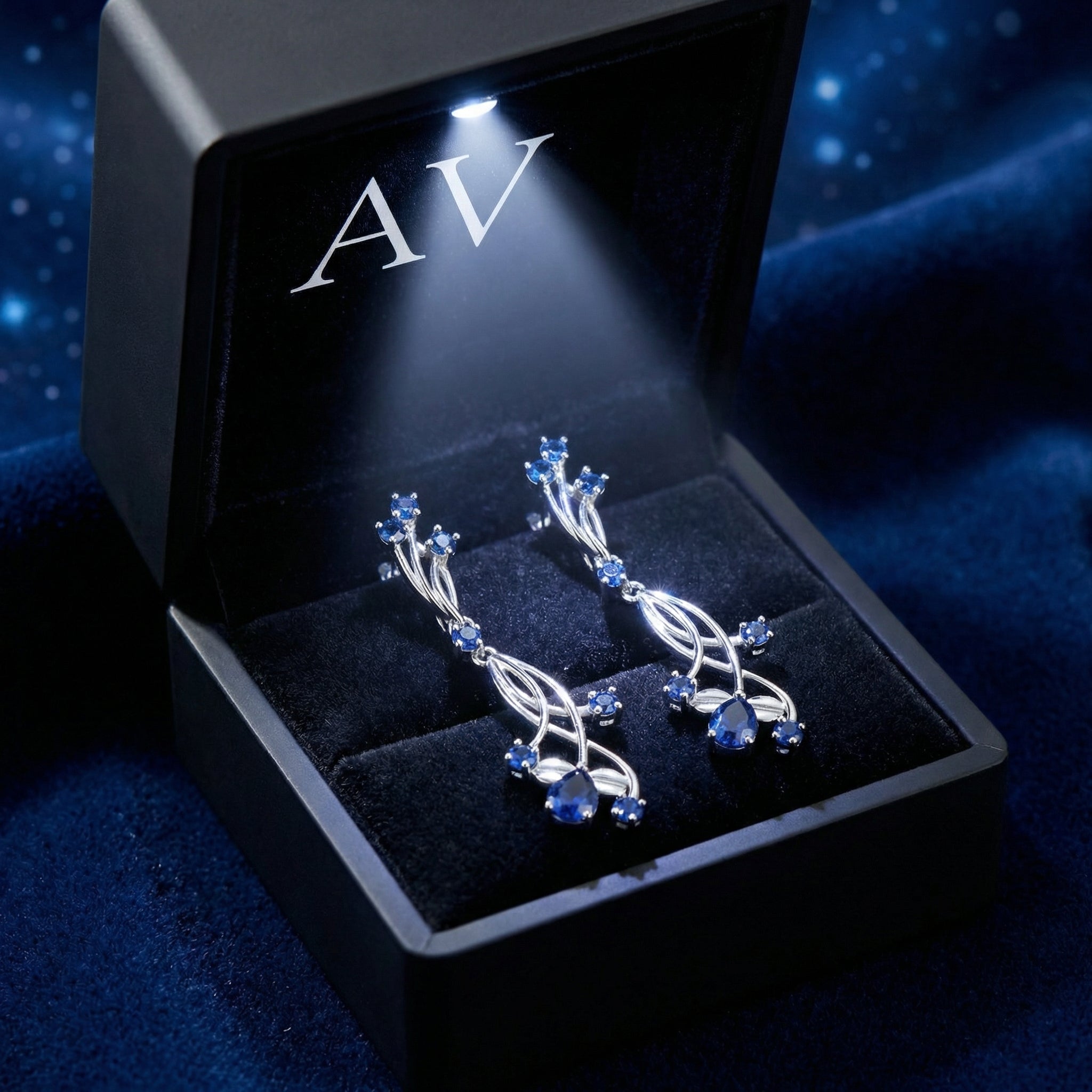 Nerise vine drop earrings with blue simulated sapphires presented in a lighted black jewelry gift box.
