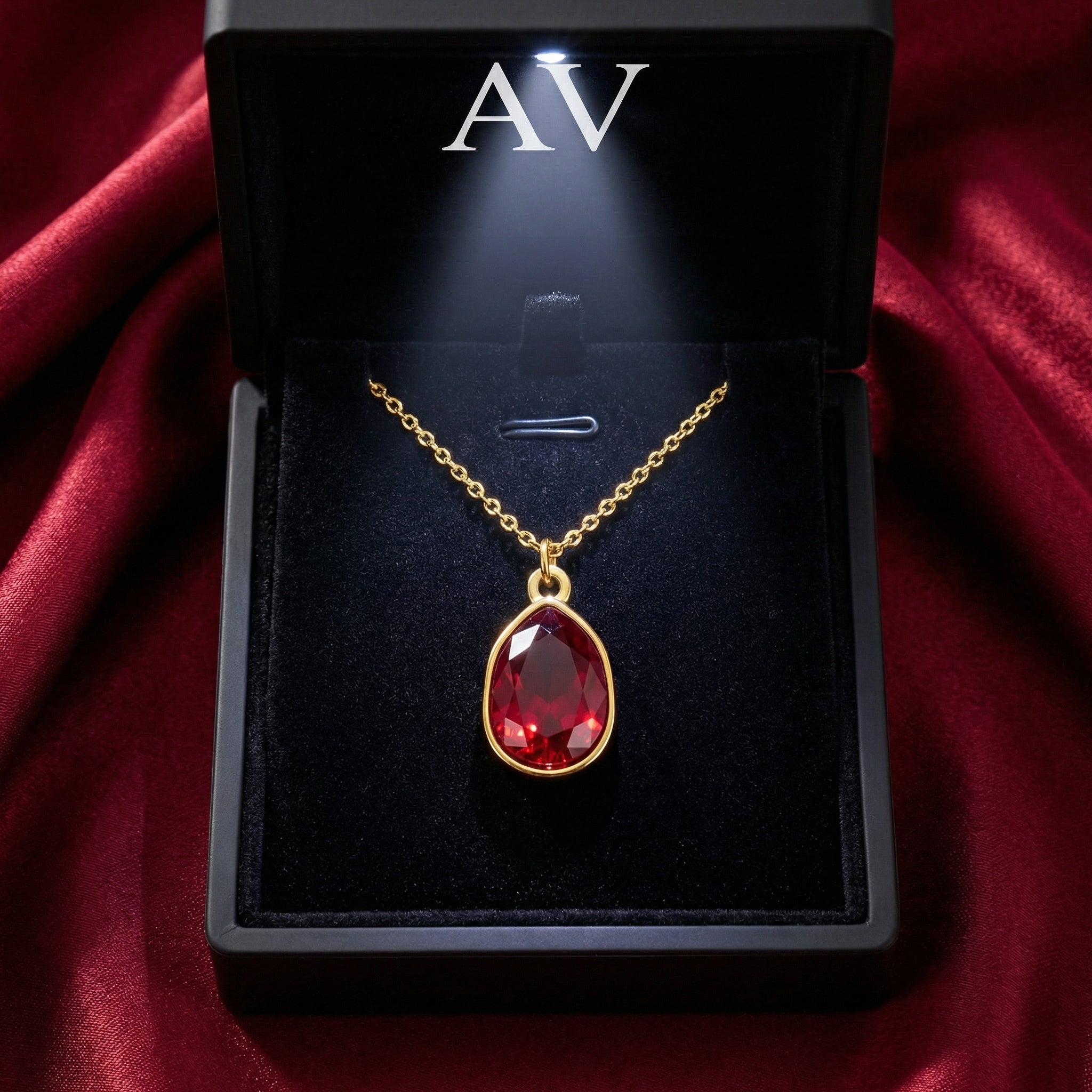 Faceted pear cut simulated ruby necklace in gold-toned stainless steel inside a lighted black gift box.