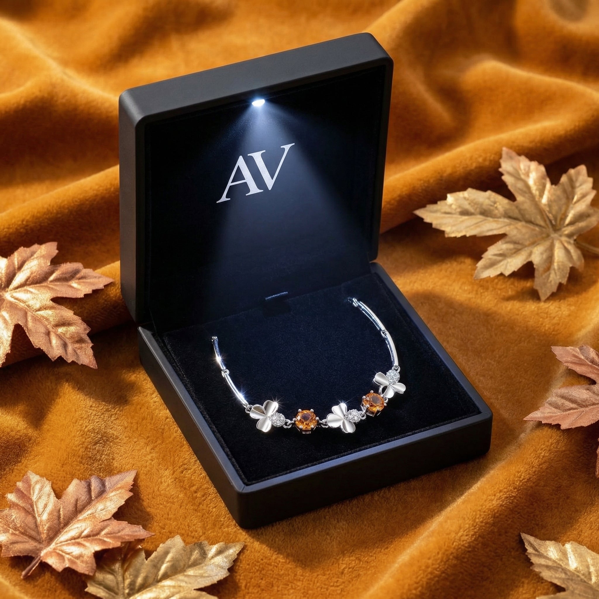 Sterling silver clover bracelet with round honey simulated topaz inside a black LED-lit jewelry box on velvet fabric.