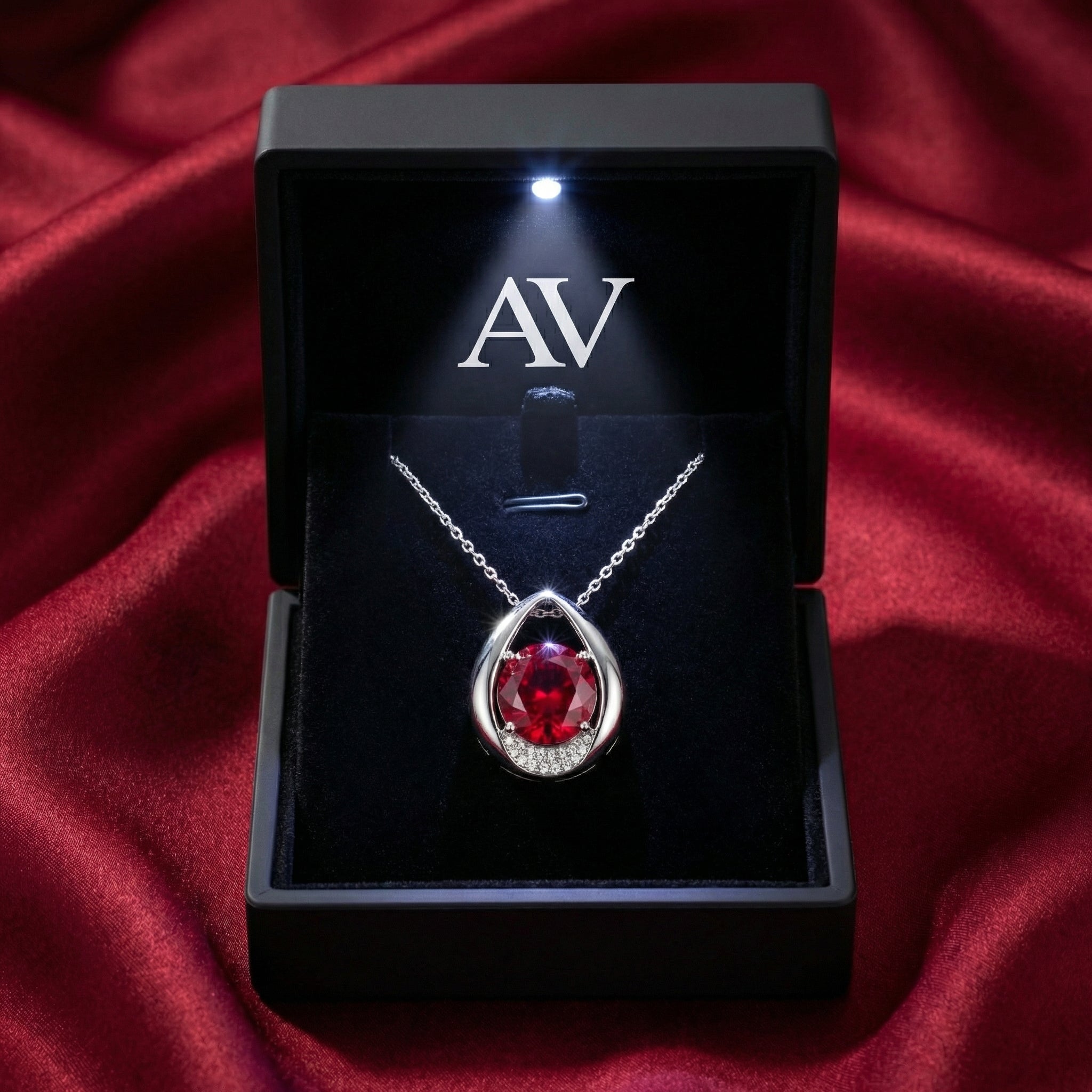 Round simulated ruby pear necklace in a black LED-lit jewelry gift box on red silk background.