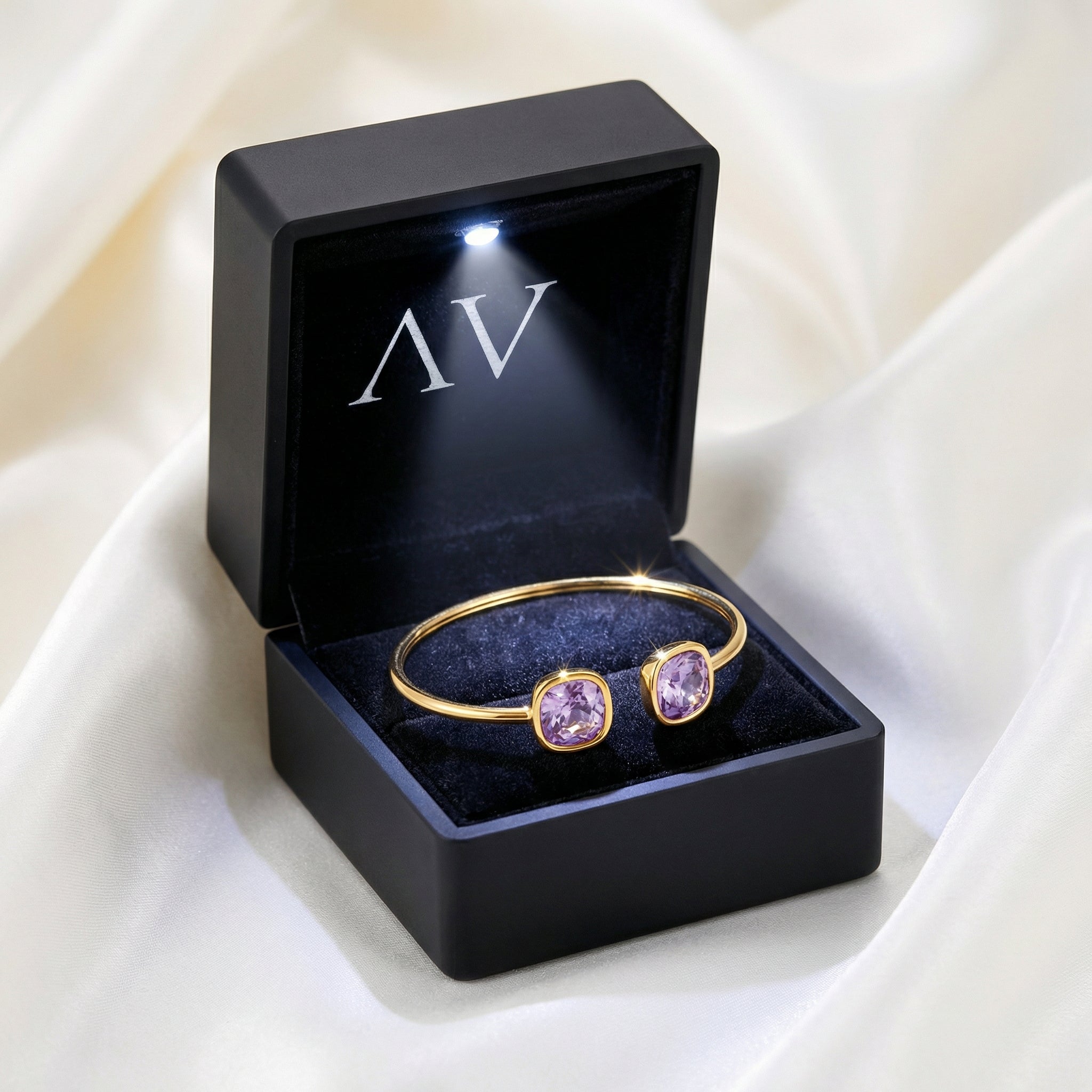 Gold Aurelia bangle with simulated amethyst stones in a black lighted jewelry box on white fabric.