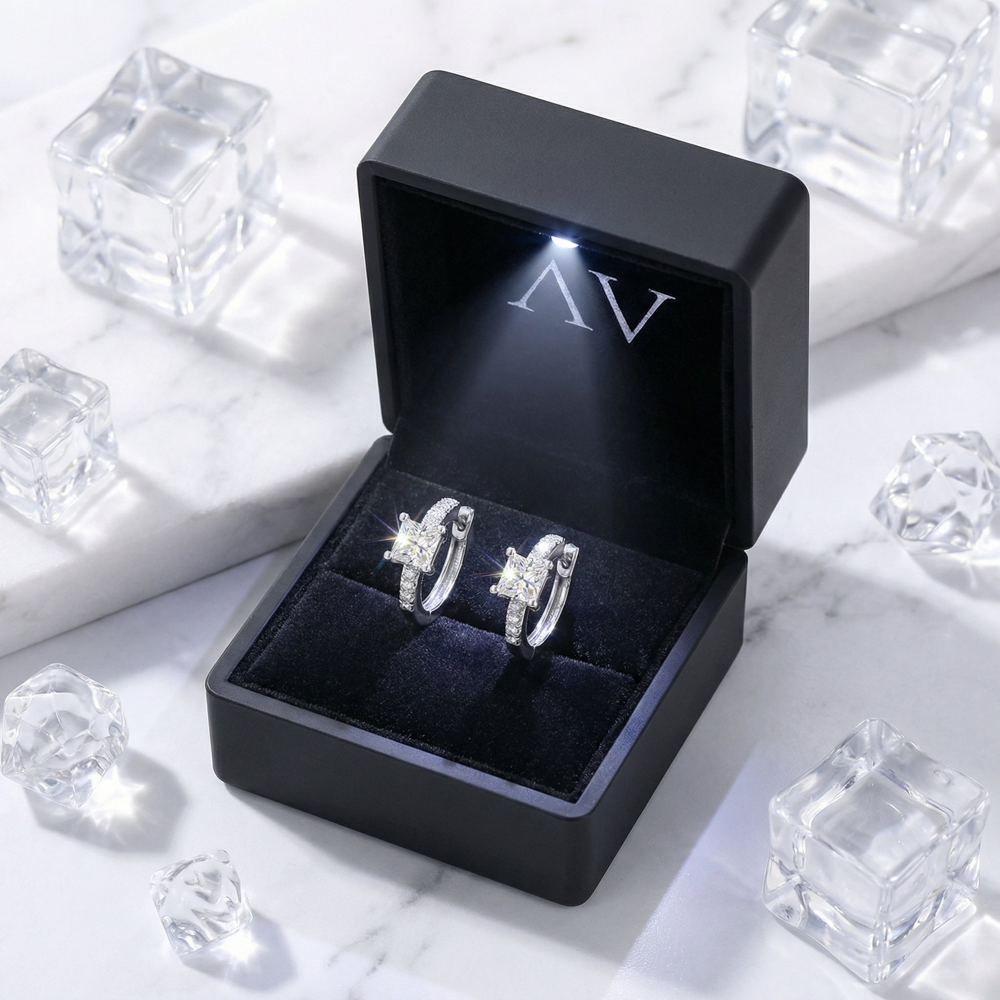 Princess-cut simulated diamond huggie earrings in a black LED-lit jewelry box on a marble surface.