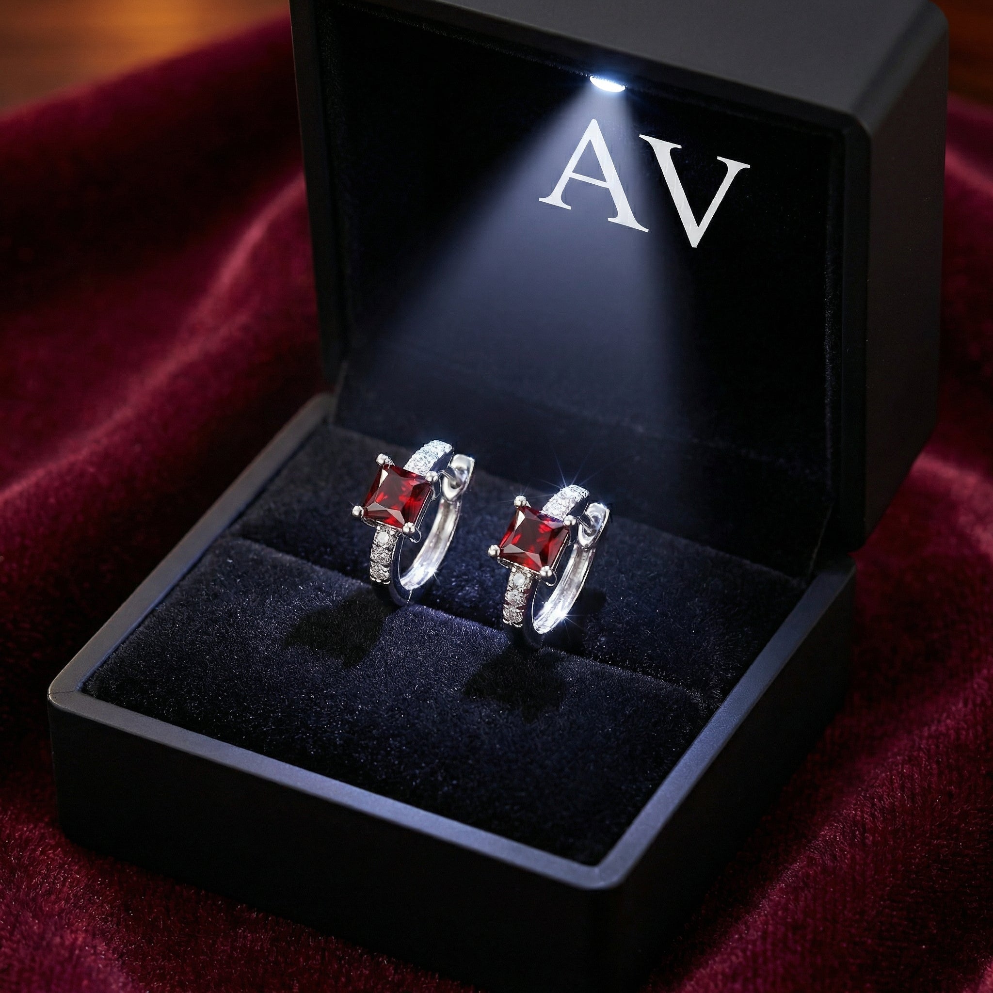 Red garnet sterling silver earrings presented in a black lighted gift box with AV branding on red velvet.