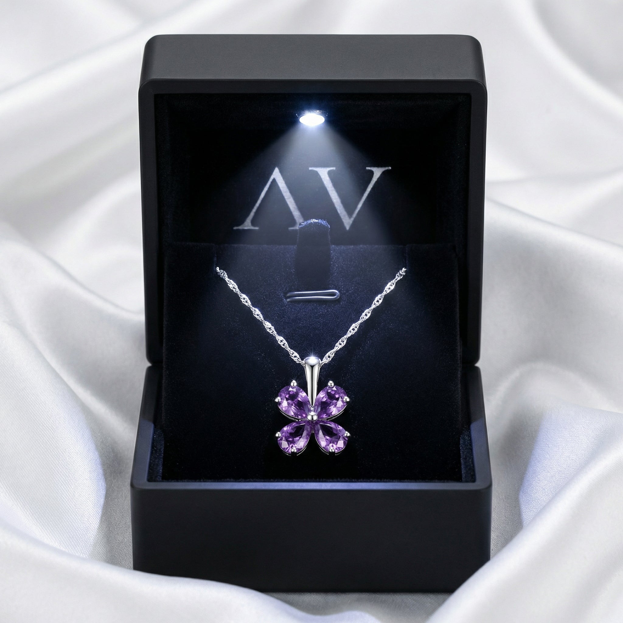 Amity clover necklace with purple simulated amethysts presented in a black lighted gift box on white silk fabric.