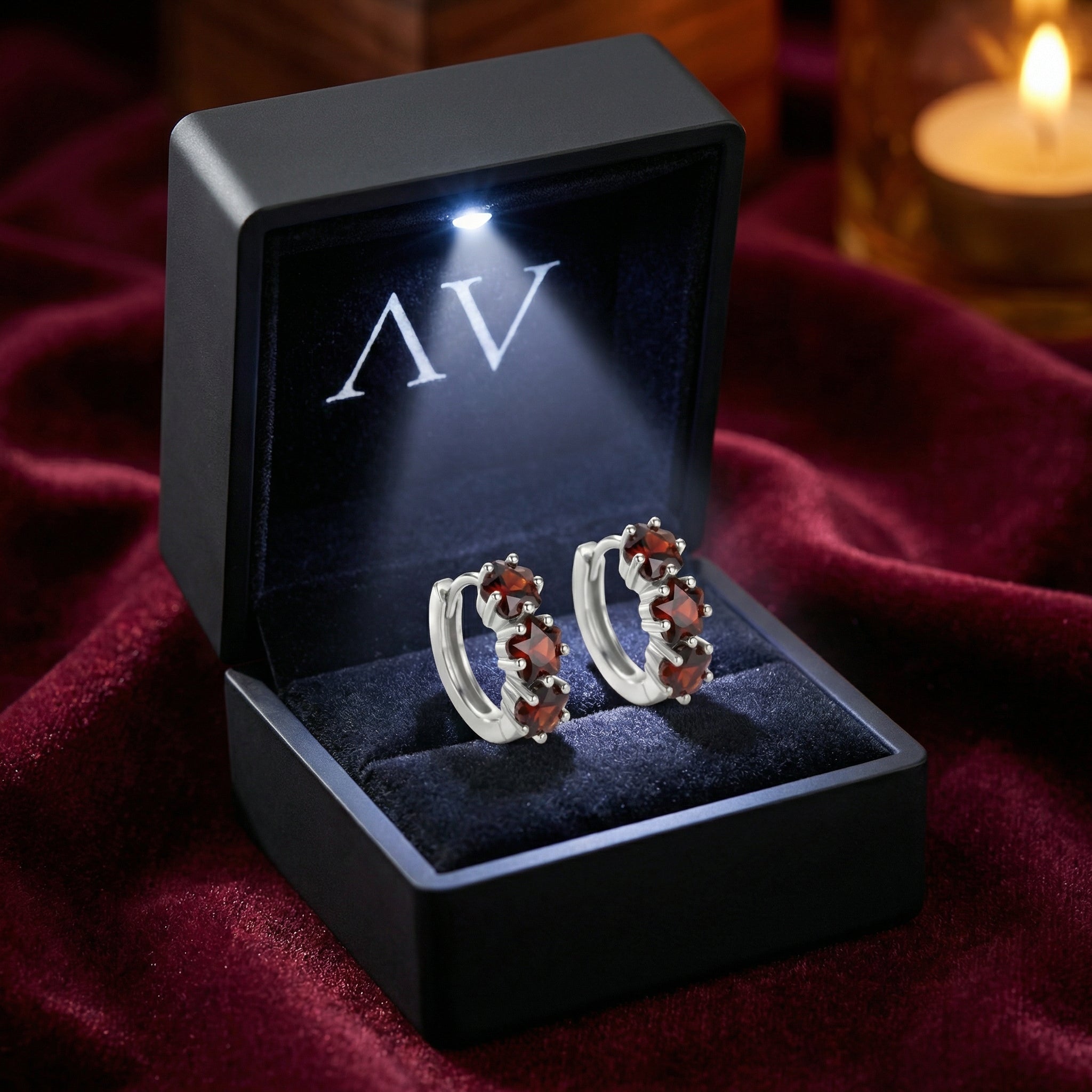 Angled view of S925 sterling silver huggie earrings with star-cut simulated garnets in a lighted gift box.