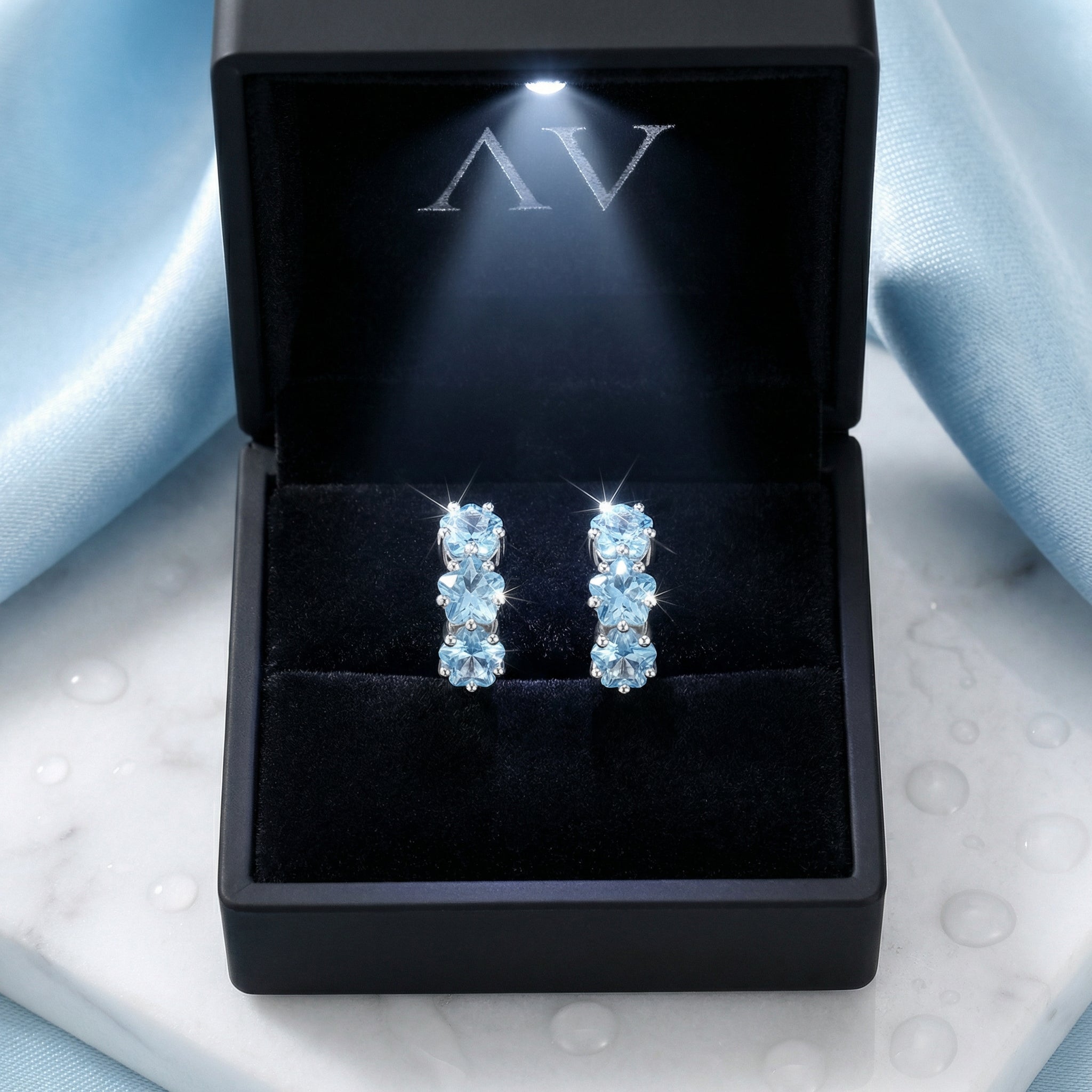 Pair of sterling silver star-cut aquamarine hoop earrings presented in a black illuminated jewelry gift box.