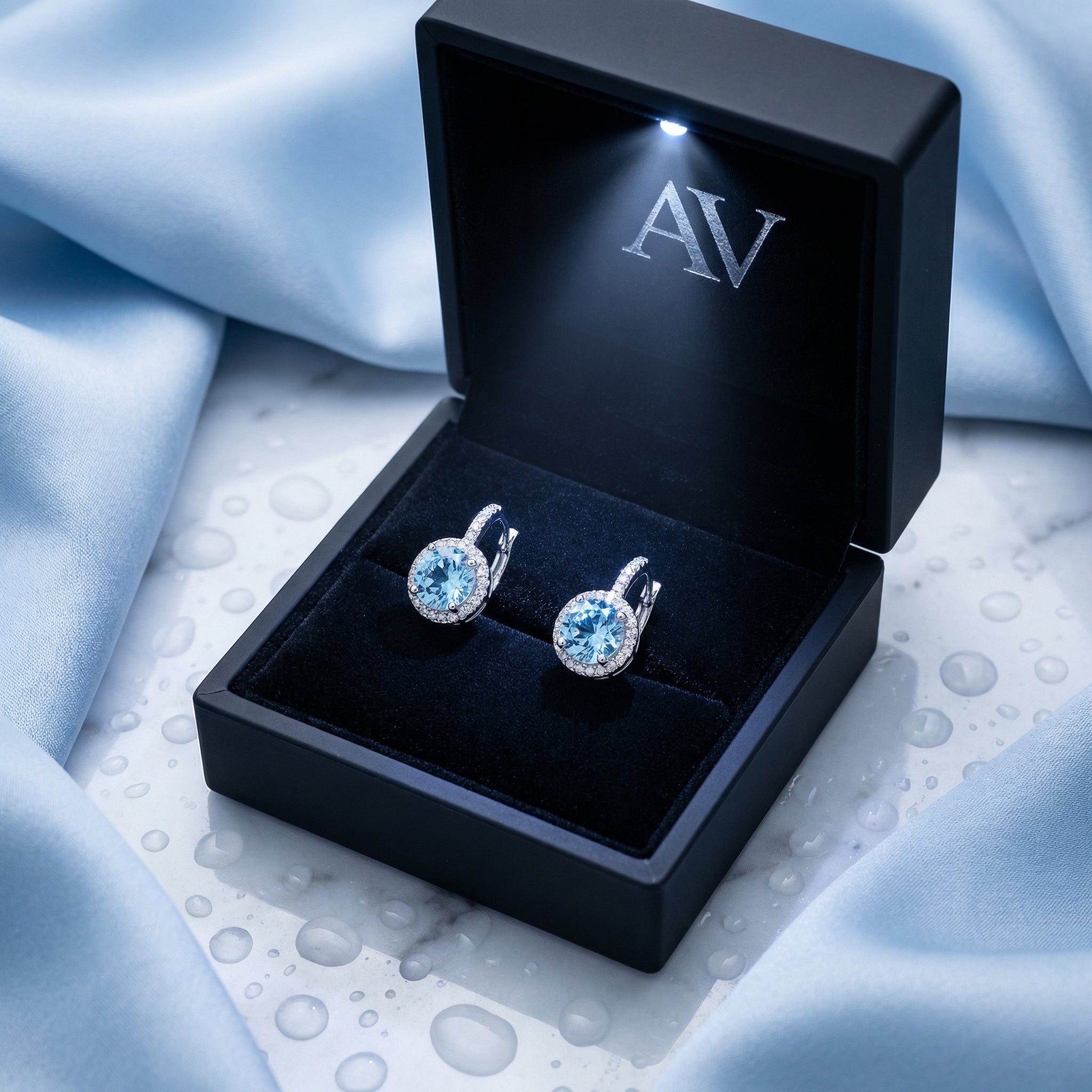 Sterling silver round cut light blue simulated aquamarine halo earrings in a black LED-lit jewelry gift box.