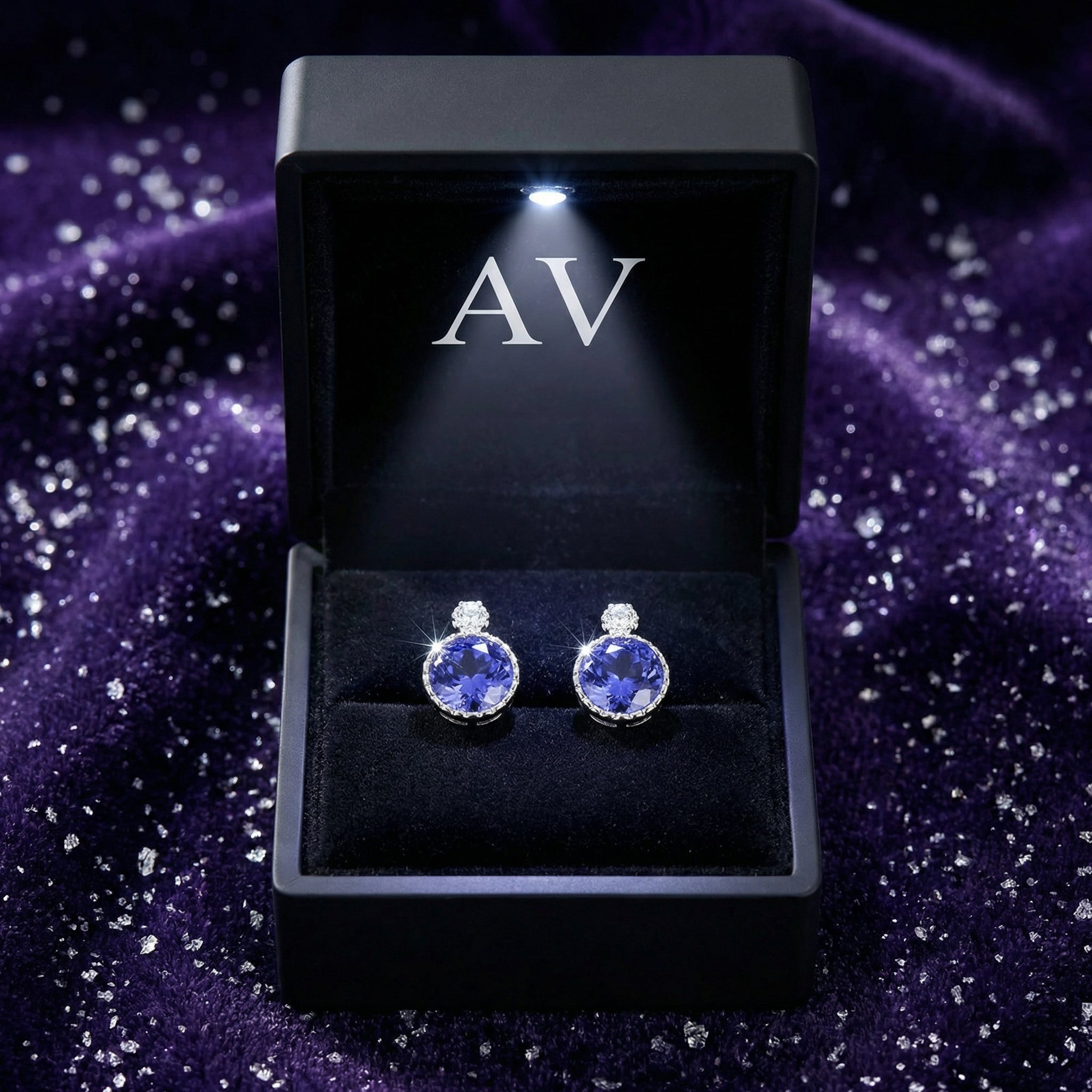 Pair of round simulated tanzanite sterling silver earrings in a lighted black AV jewelry gift box.