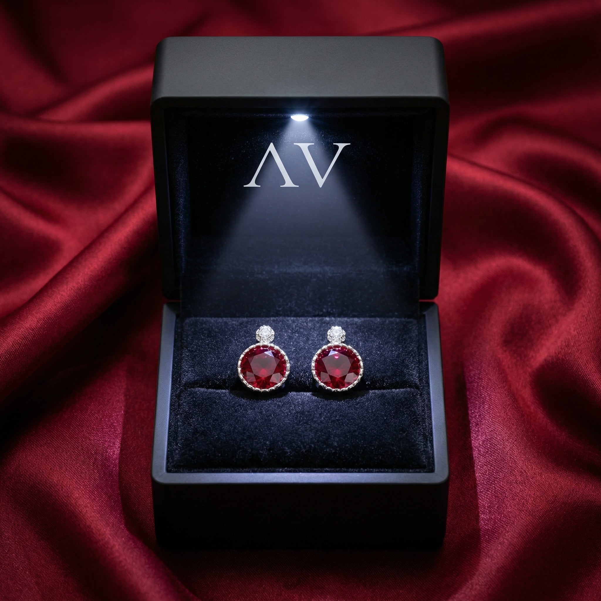 Simulated ruby stud earrings in S925 sterling silver inside a lighted black gift box on red satin.