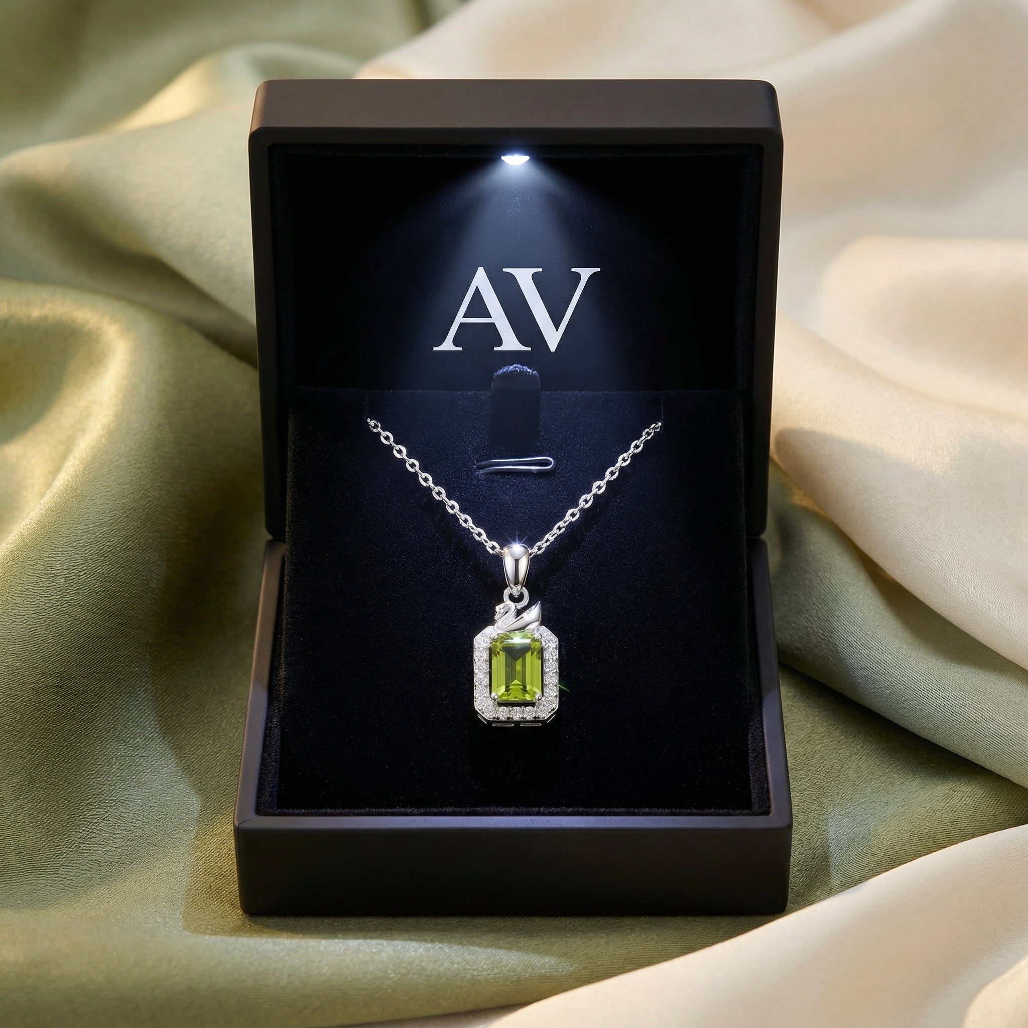 Emerald-cut peridot pendant in a black LED-lighted jewelry box with AV branding, displayed on draped silk fabric.