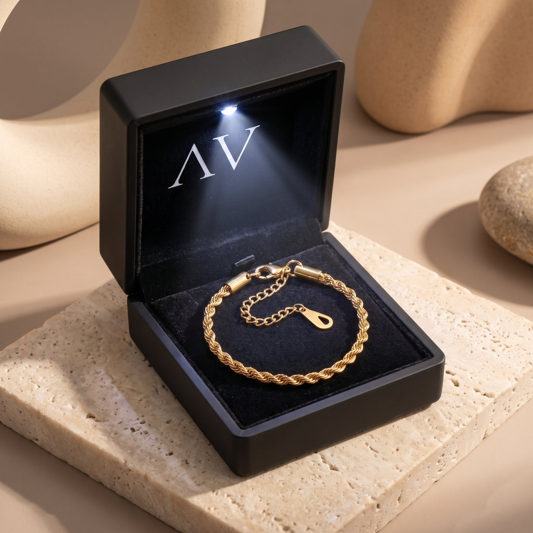 Gold rope bracelet inside a black LED-lit gift box on a stone surface.