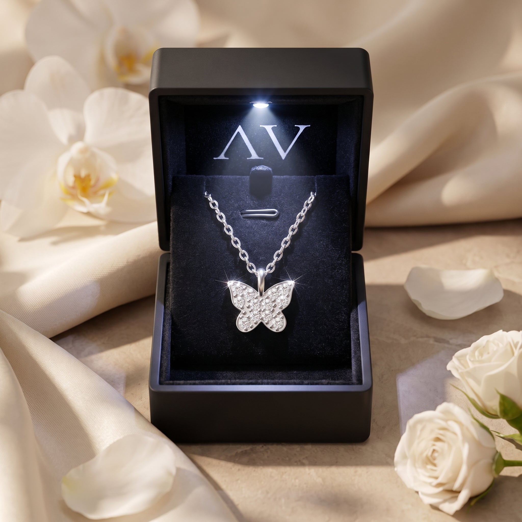 Silver moissanite butterfly necklace inside a black LED-lit gift box surrounded by white roses.