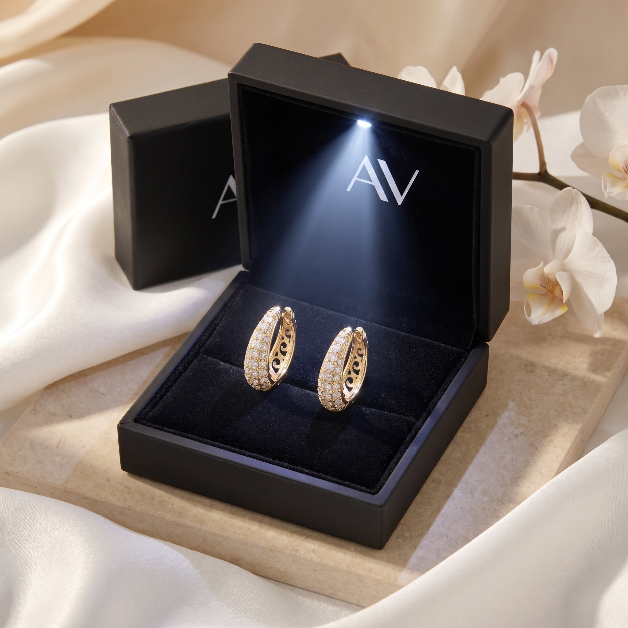 Gold moissanite hoop earrings inside a black LED-lit gift box on a silk background.
