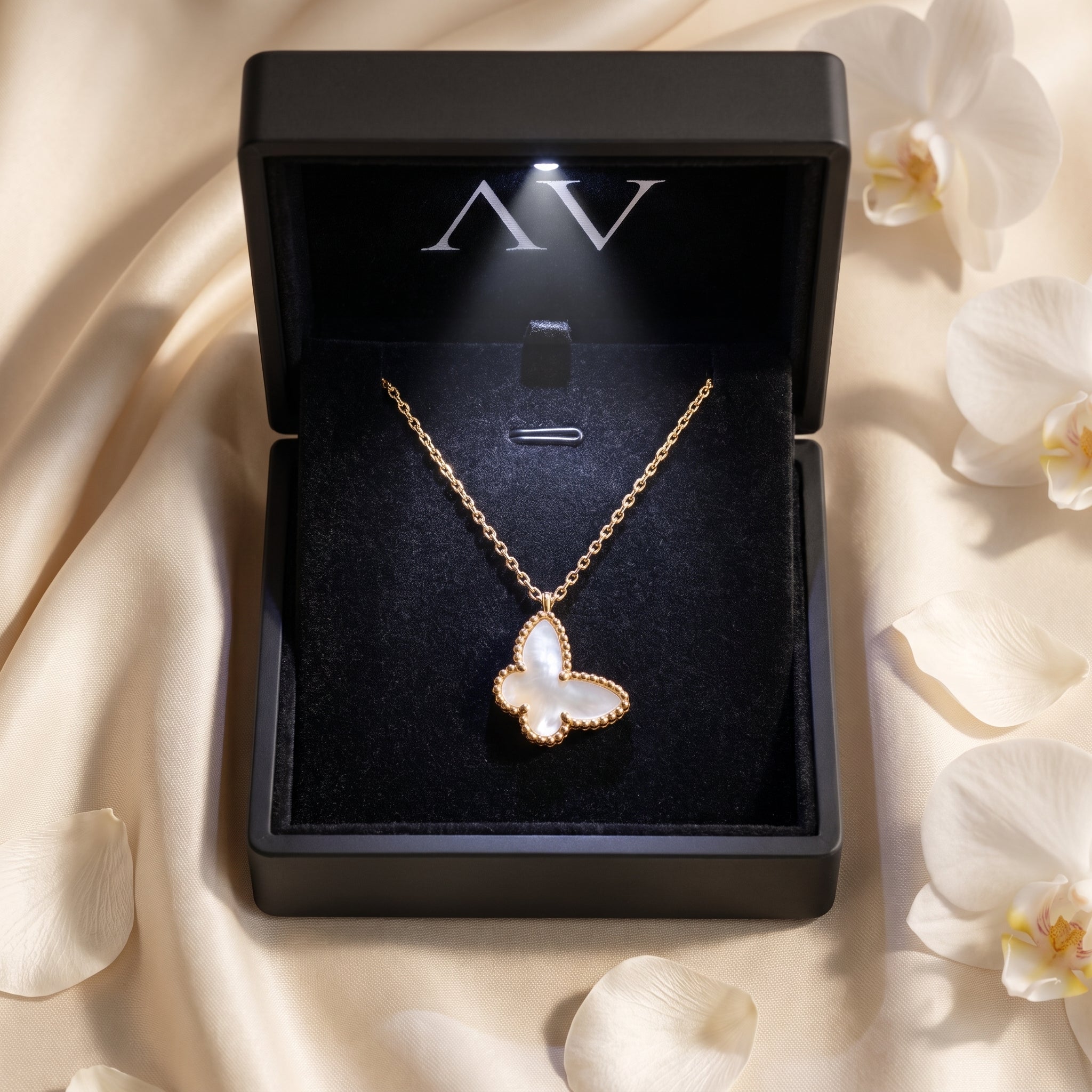 Yellow gold mother of pearl butterfly necklace inside a lighted black gift box with white orchid petals.