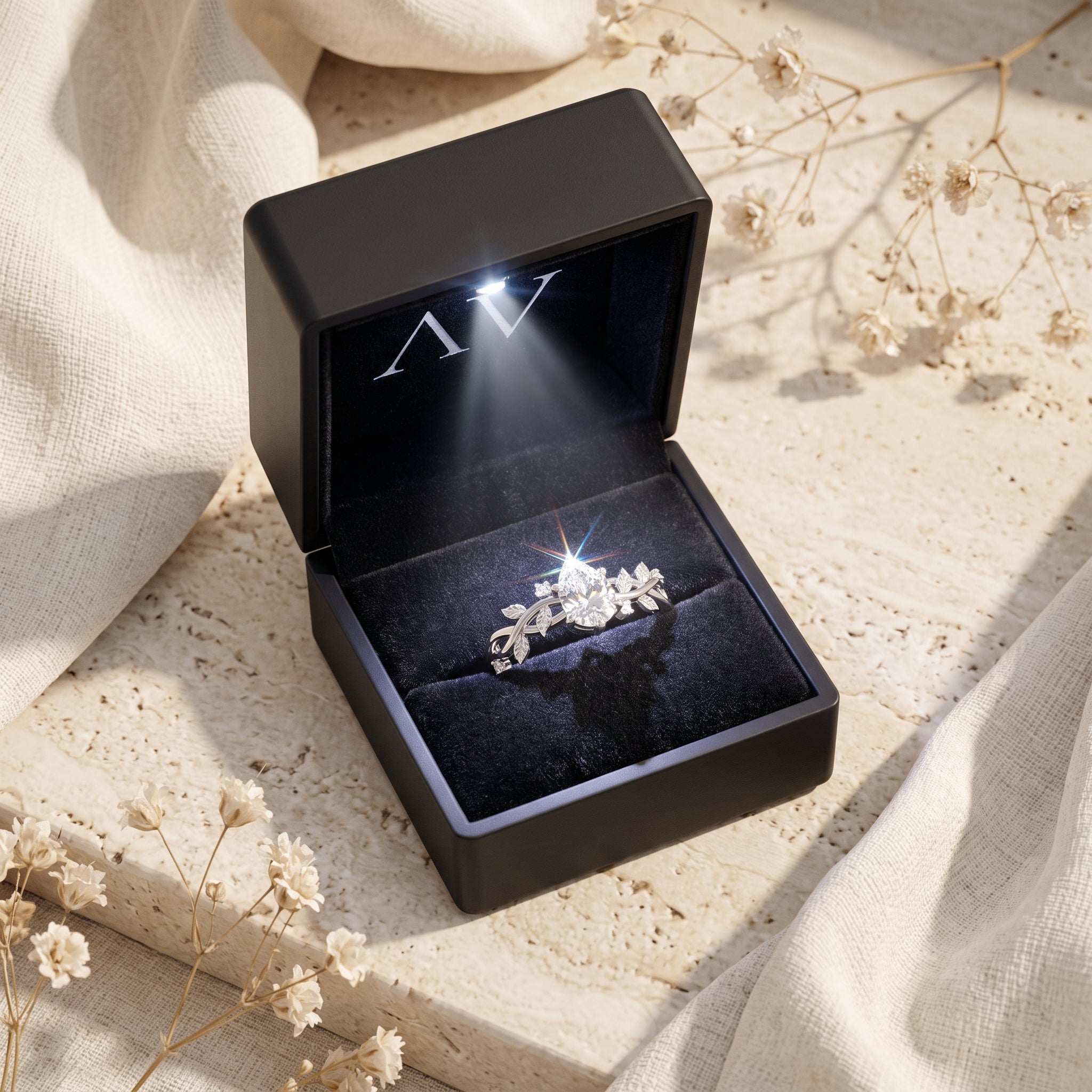 Silver pear cut moissanite ring inside a black lighted jewelry presentation box.