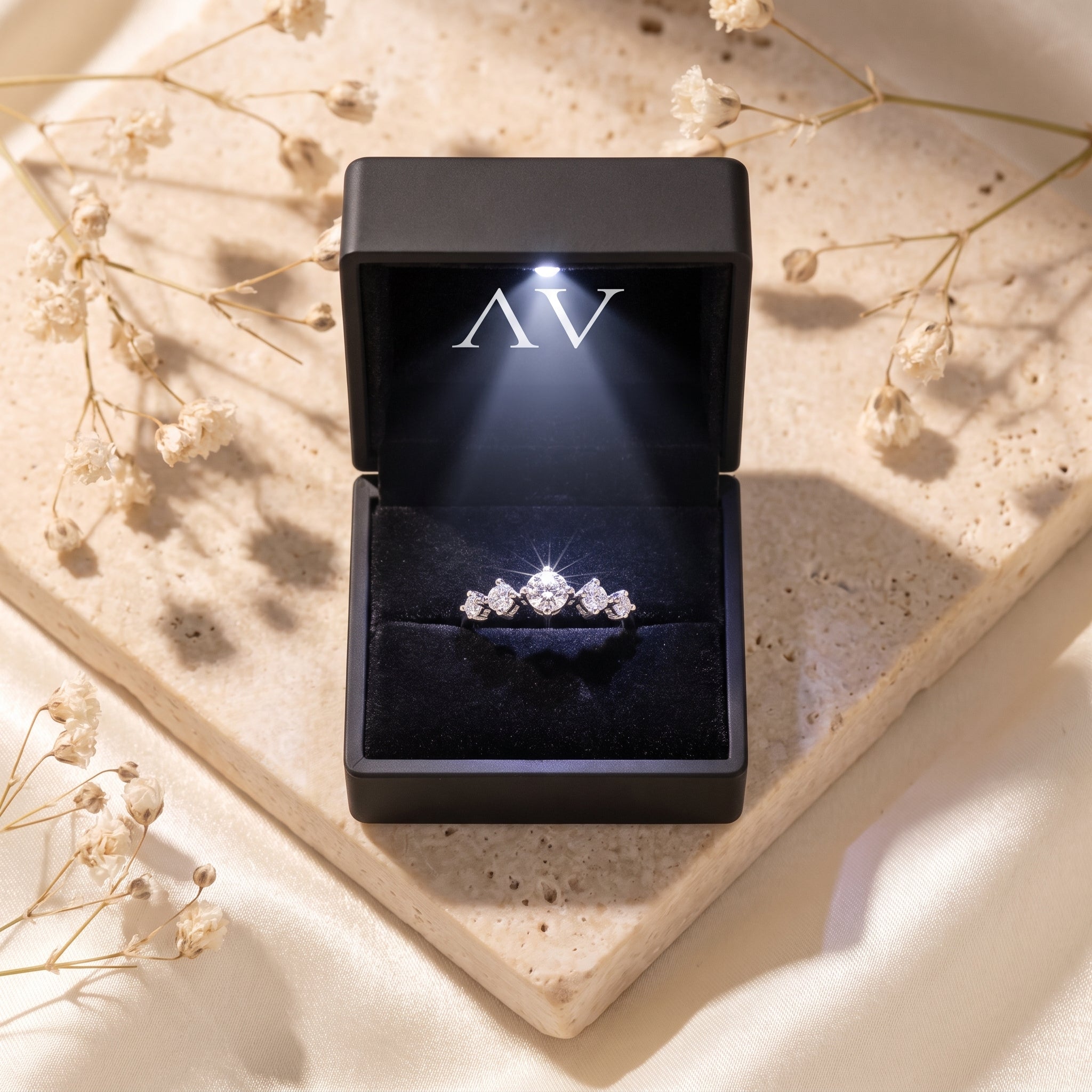 Silver moissanite ring in a lighted black jewelry box.