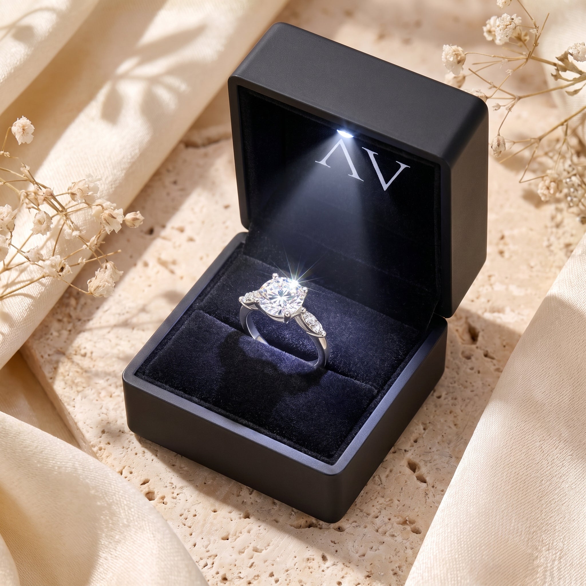 Claudine round cut solitaire ring presented in a black LED-lighted gift box on a soft fabric background.