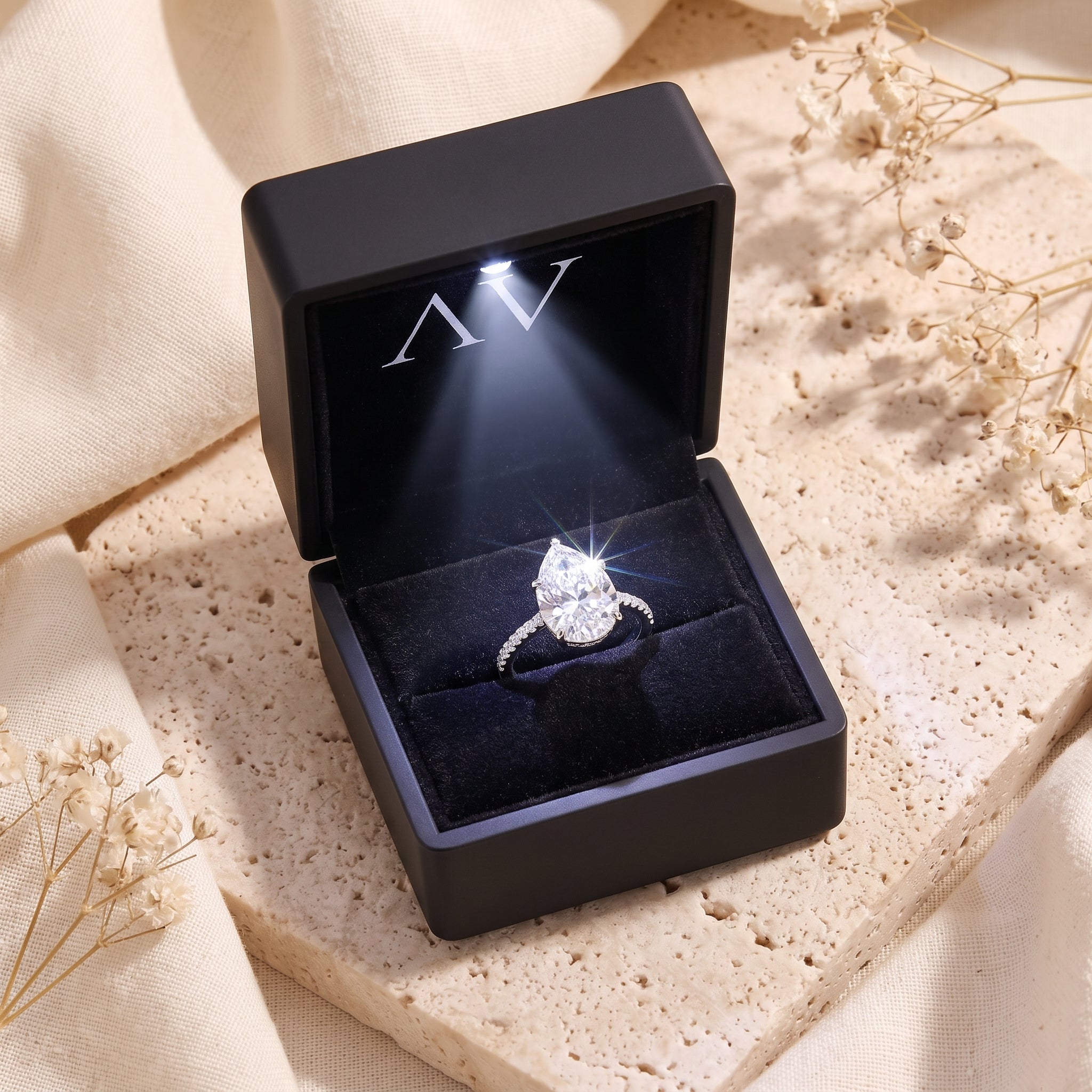 Pear-cut simulated diamond ring inside a black illuminated luxury gift box on a stone surface.
