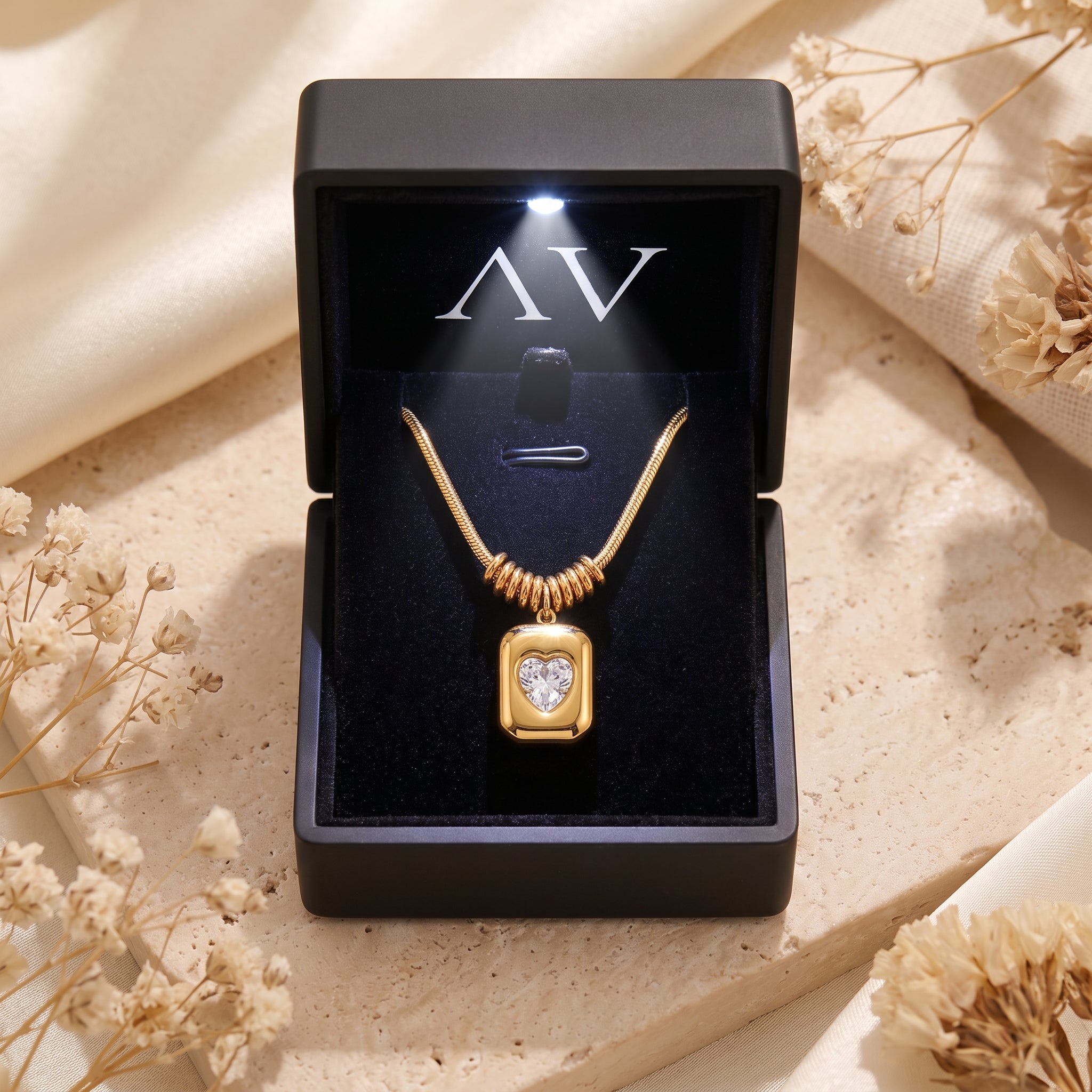 Gold Sophia Heart Necklace displayed in a black LED-lit jewelry box on a stone surface with flowers.