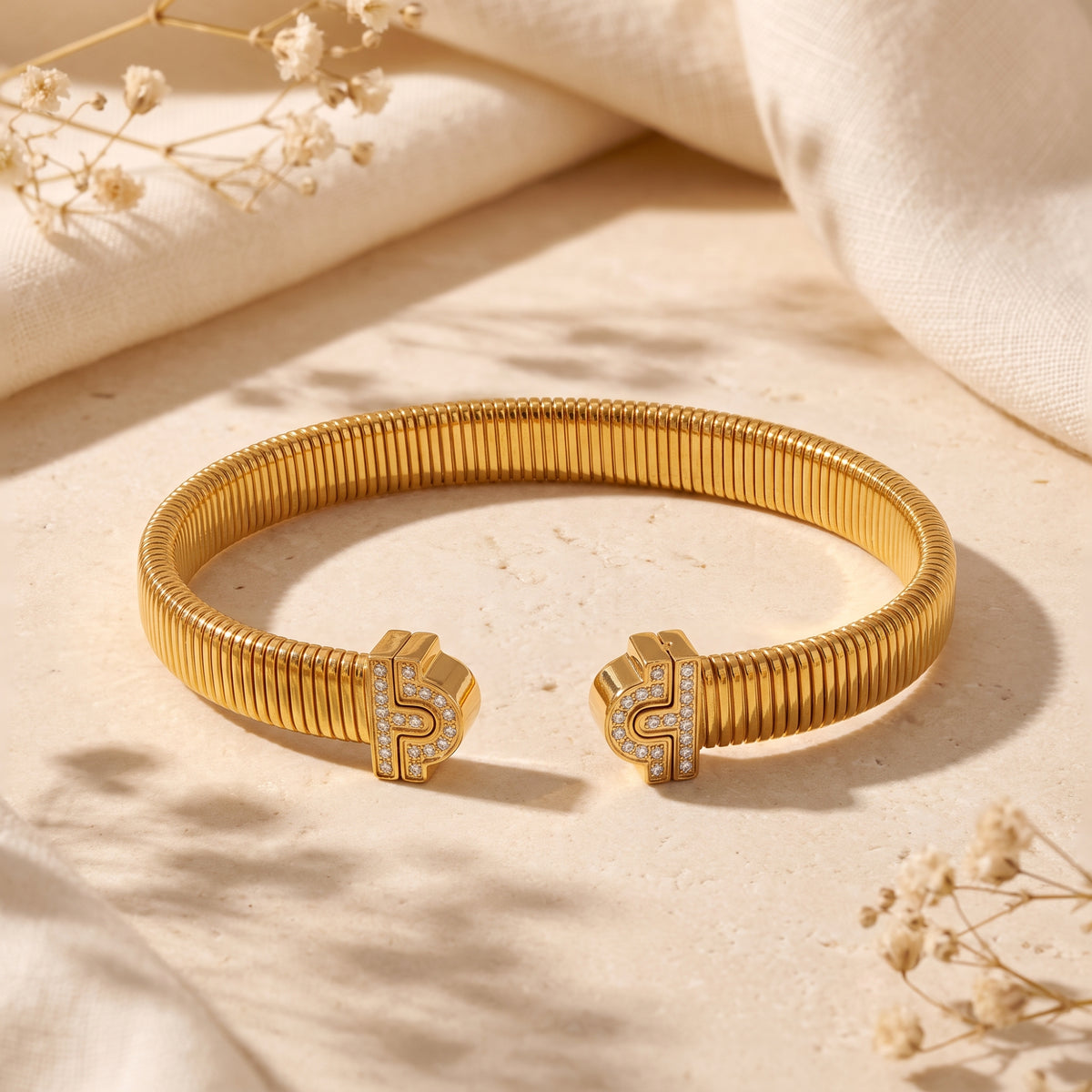 Gold-finish ribbed open cuff bracelet with pavé cubic zirconia ends resting on a pale stone surface.