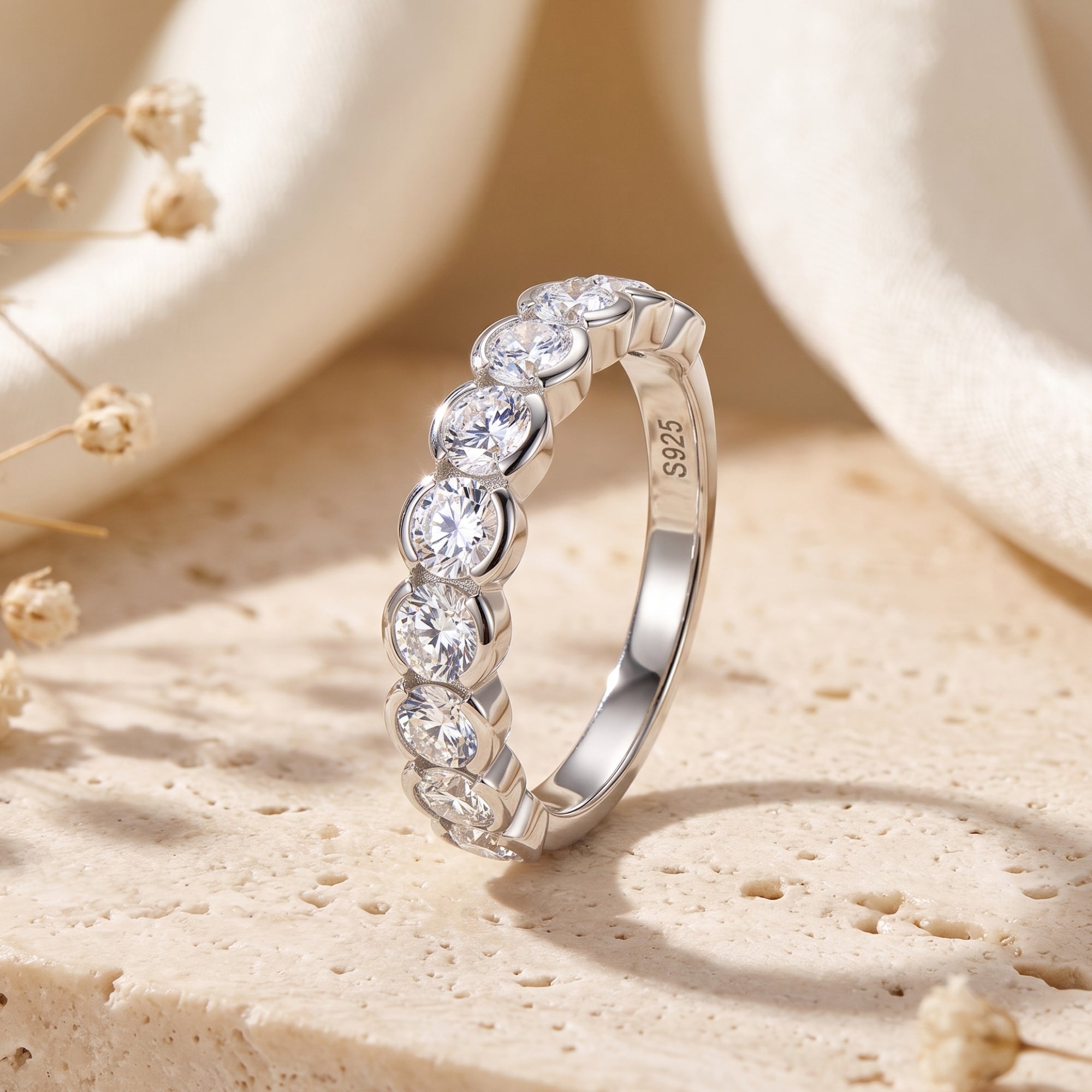 Round-cut simulated diamond bezel eternity ring in S925 sterling silver on a textured stone lifestyle background.