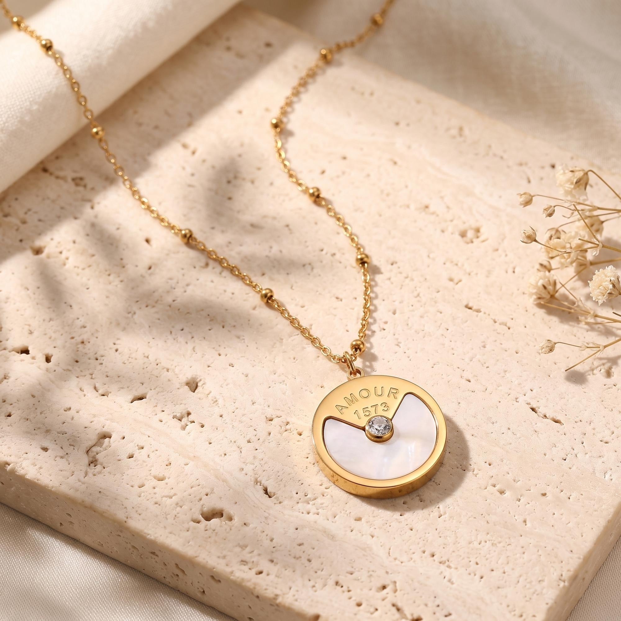 Gold pendant necklace with mother-of-pearl and round CZ on a textured stone slab.