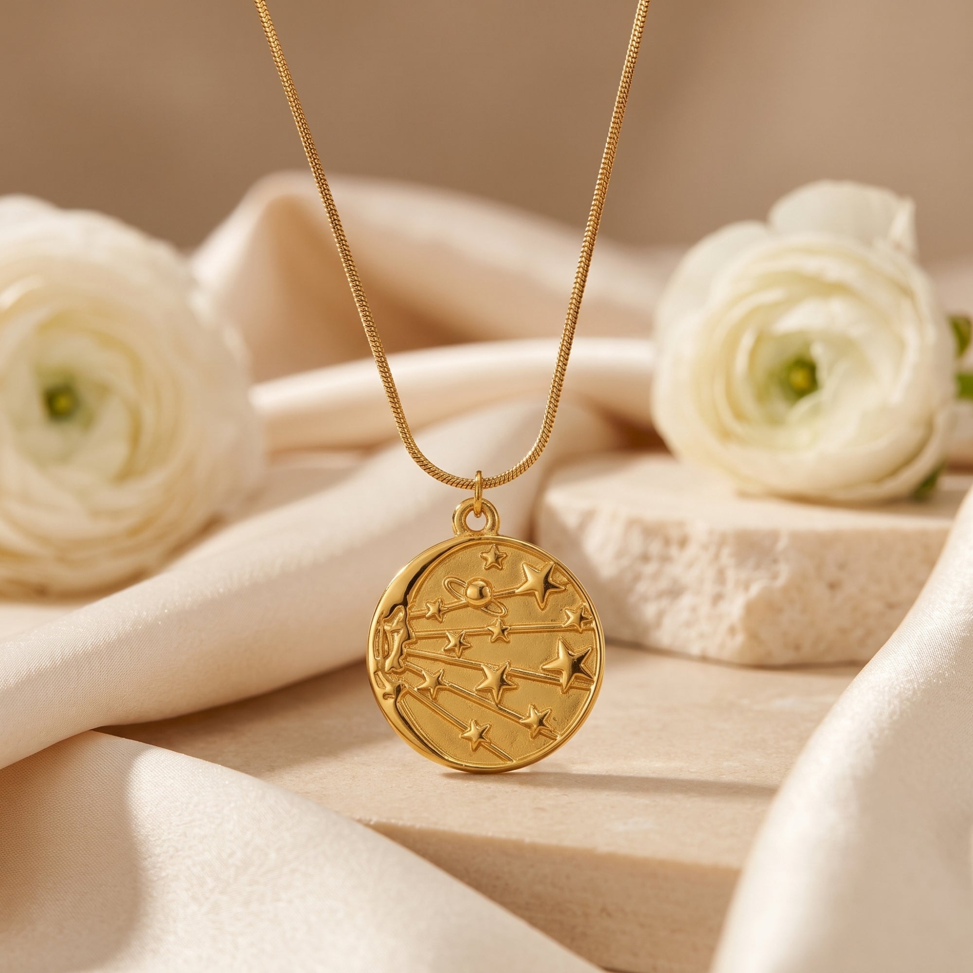 18K gold celestial medallion necklace on snake chain, styled with silk and white flowers.