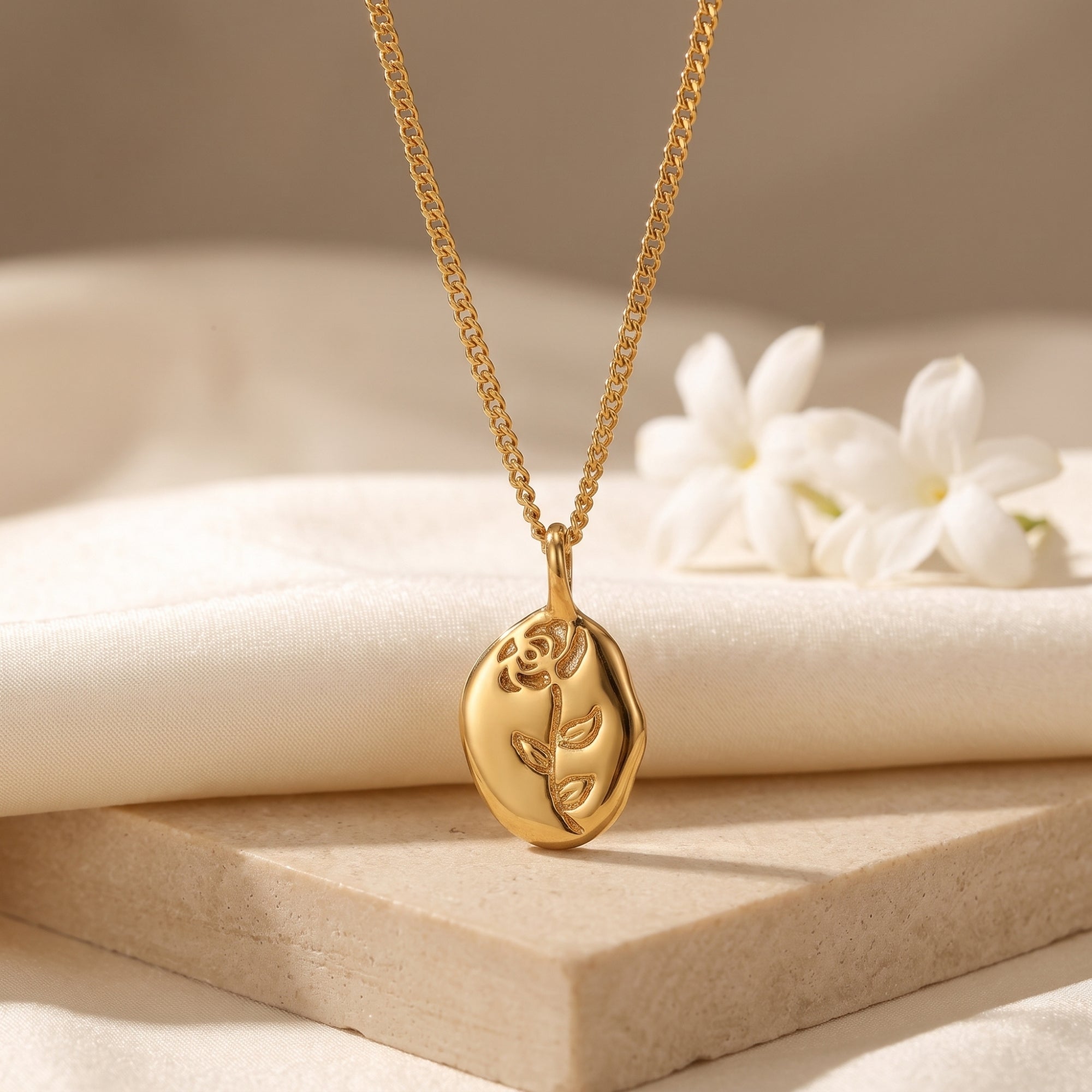 18K gold finish rose pendant necklace displayed on a stone block with white flowers.