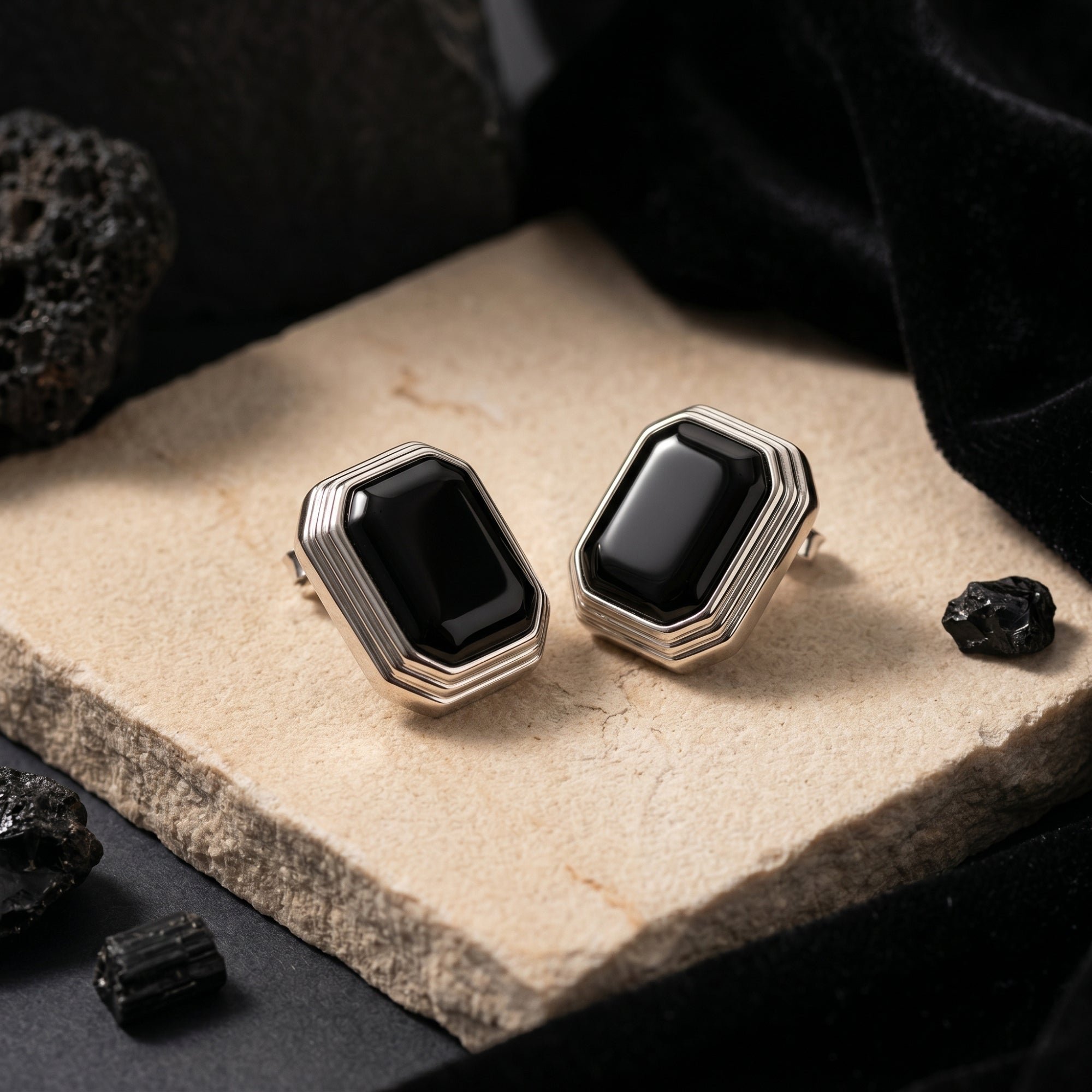 Square cut natural black onyx earrings in silver, displayed on a stone slab with black velvet and volcanic rocks.