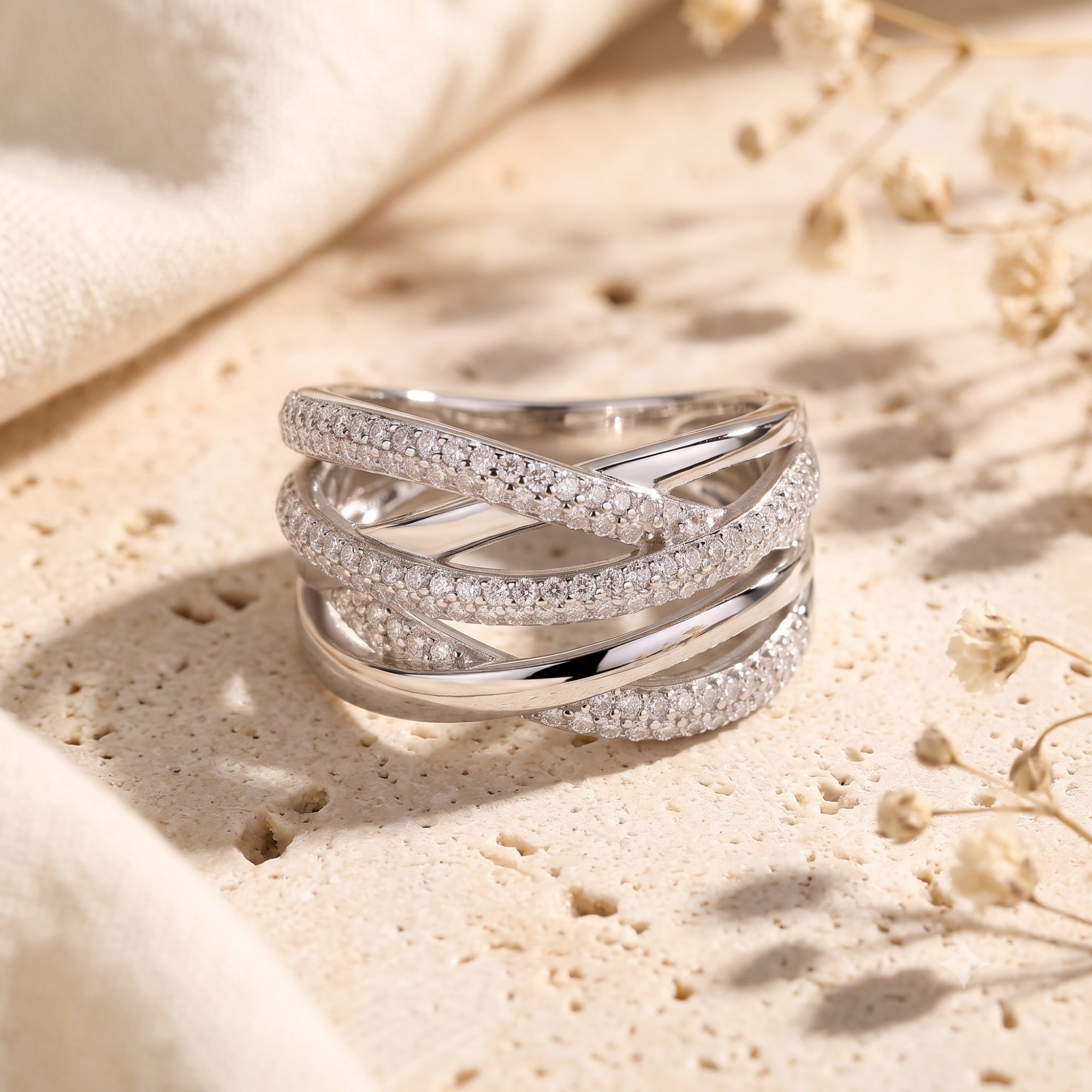Silver crossover ring with pavé simulated diamonds on a stone surface with dried flowers.