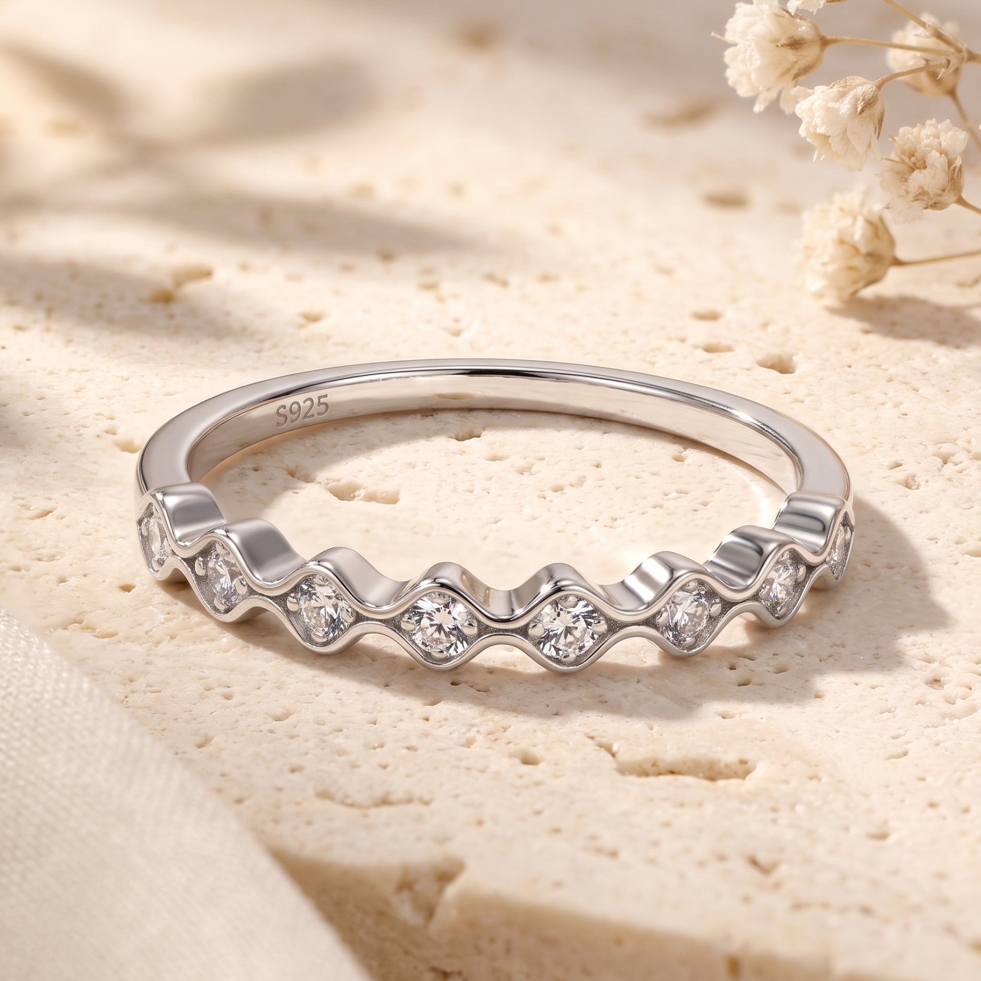 Wavy sterling silver eternity ring with round simulated diamonds on a textured stone surface.