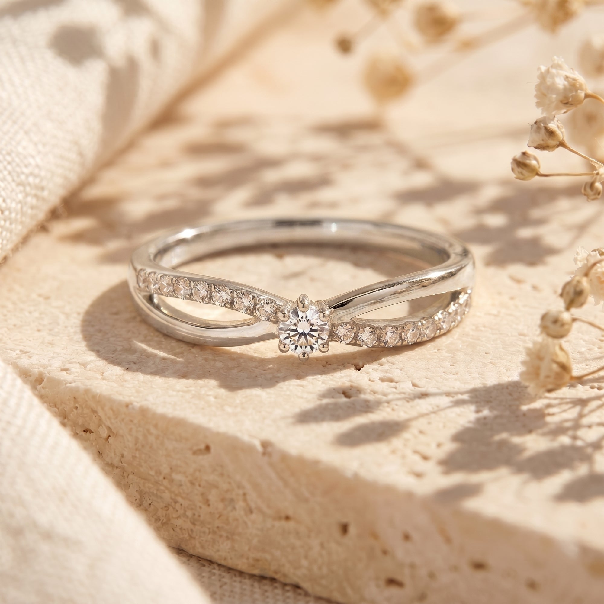 Silver bypass promise ring with round-cut moissanite on a stone surface.