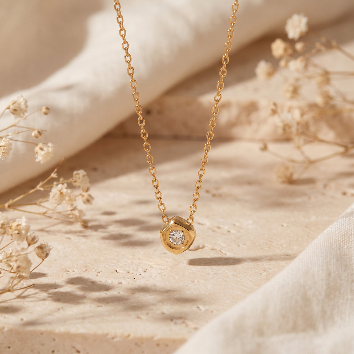 Gold-tone hexagon pendant with a clear cubic zirconia stone hanging over a textured beige stone surface.