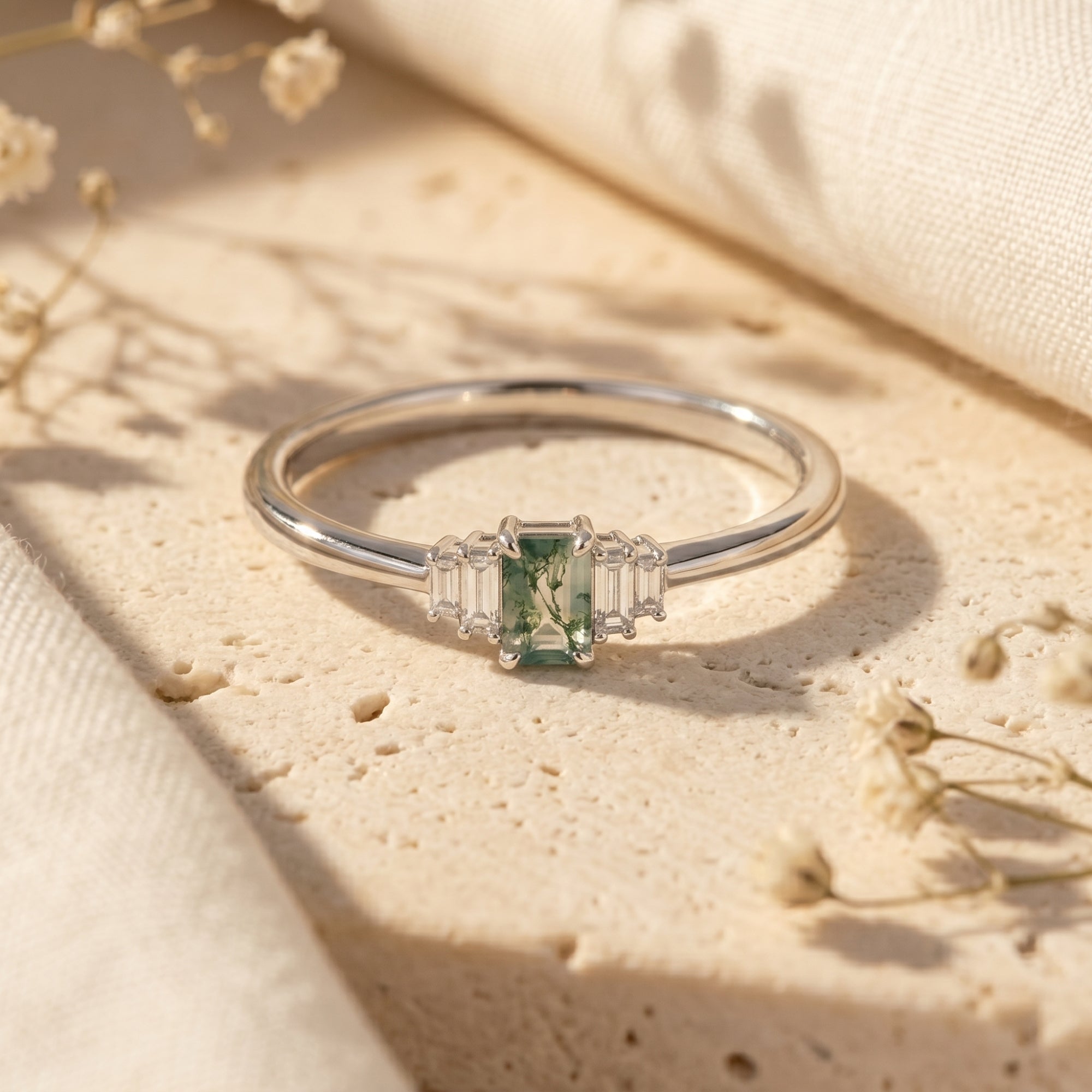 Emerald-cut green moss agate ring in sterling silver on a stone surface with dried flowers.