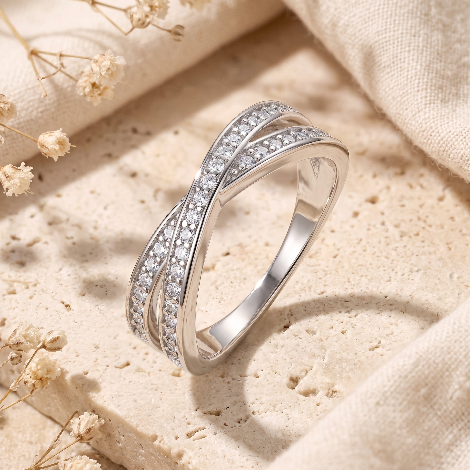 Silver crossover promise ring with cubic zirconia on a stone surface with dried flowers.