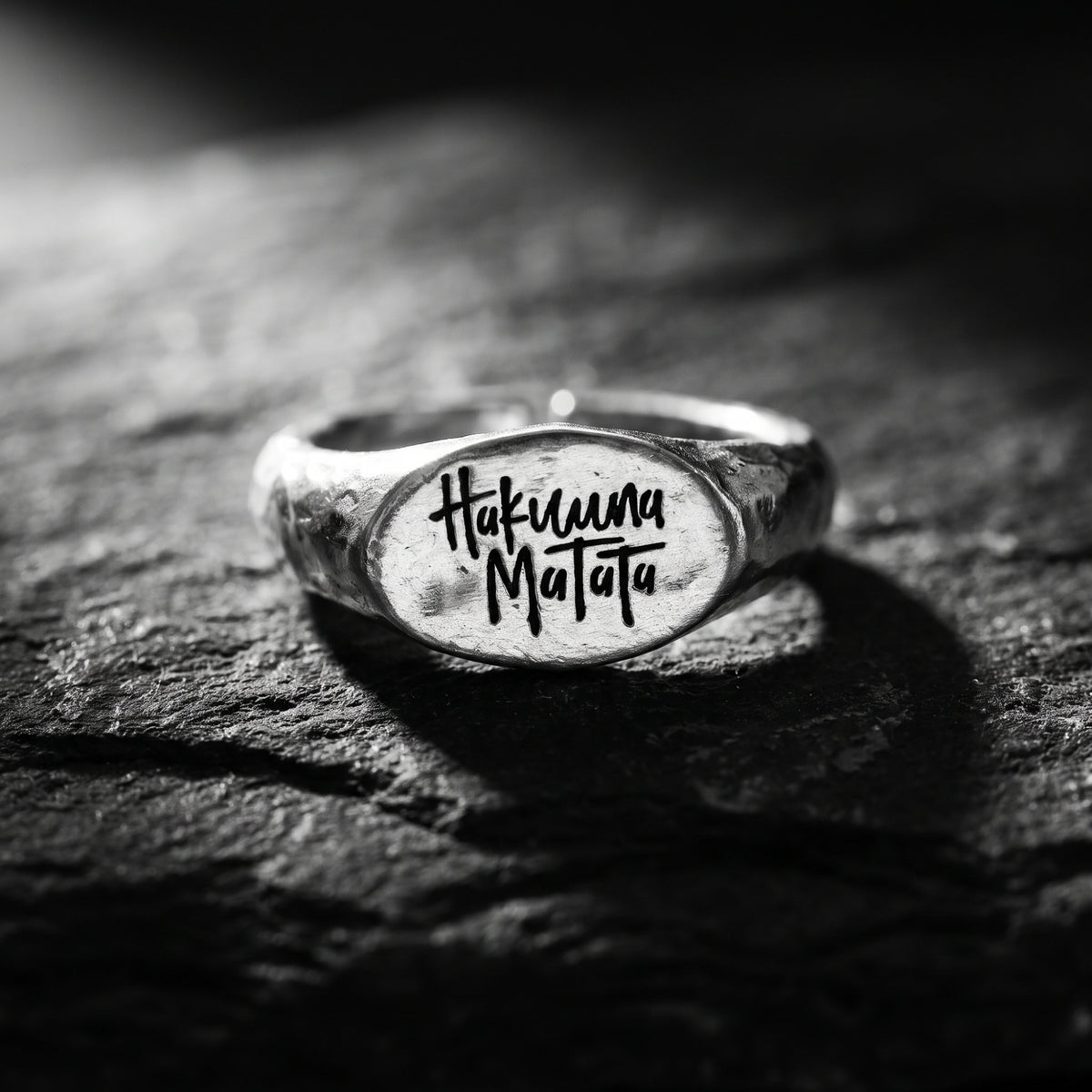 Front view of the silver oval signet ring engraved with Hakuna Matata on a dark stone surface.
