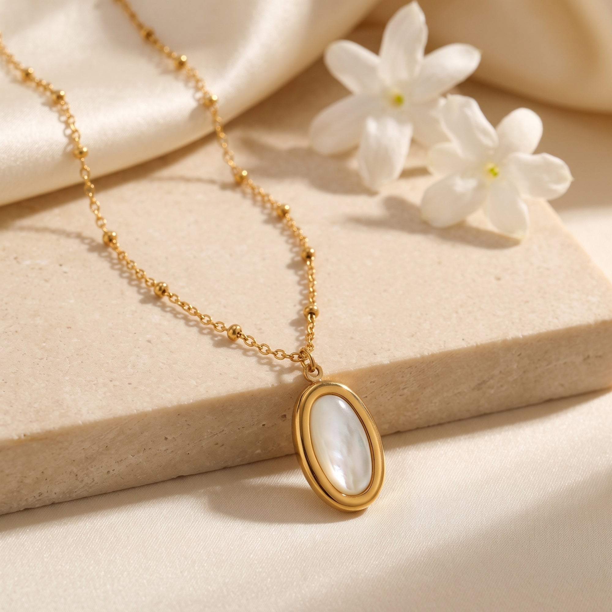 Gold mother of pearl necklace on beaded chain with white flowers.