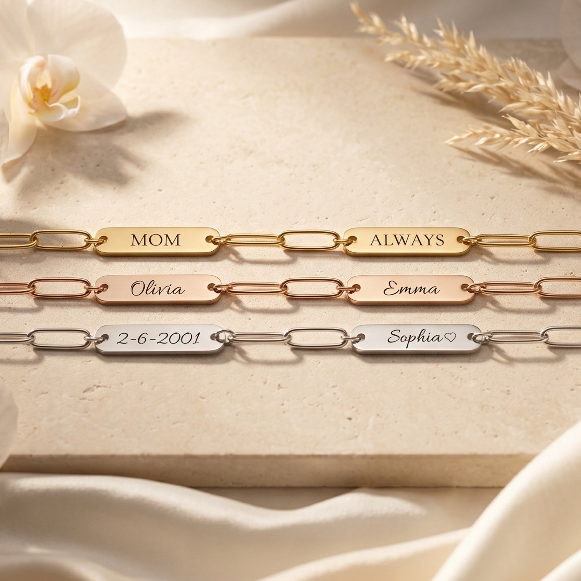 Gold, rose gold, and silver personalized link bracelets with engraved name plates on a stone background.