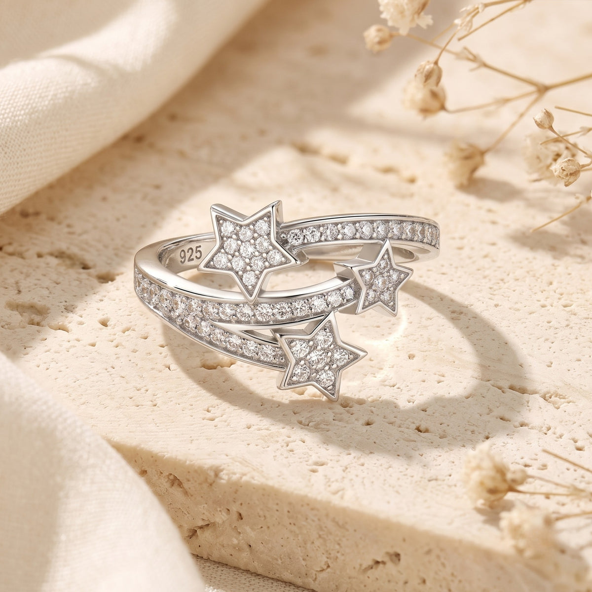 Close-up of the silver shooting star bypass ring with three pave-set stars on a cream stone surface.