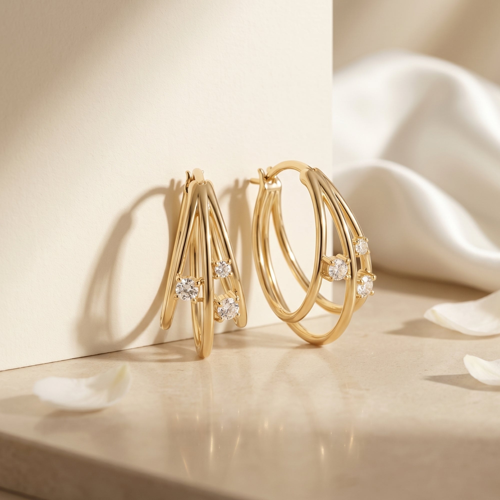 Gold triple hoop moissanite earrings on a stone surface with white petals.