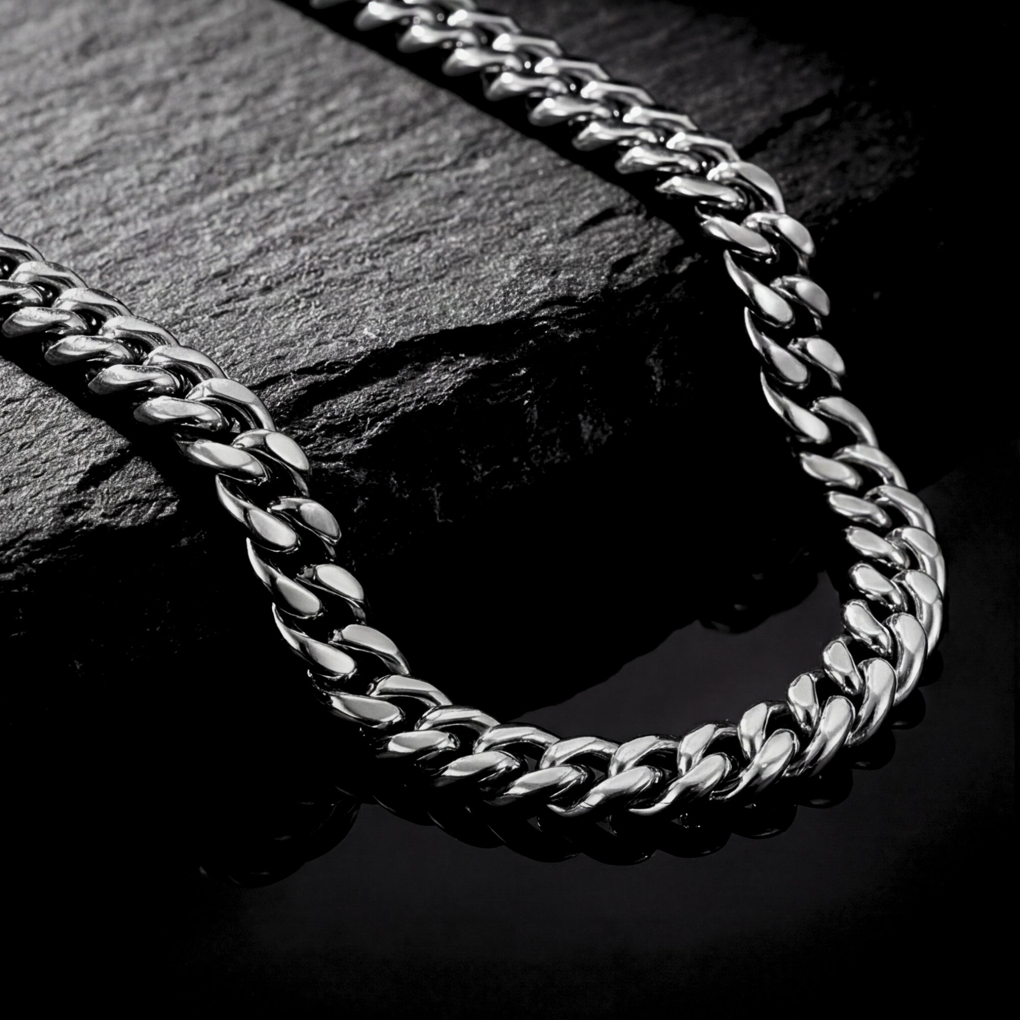 Macro view of the polished 8mm silver stainless steel Cuban links resting on a dark stone surface.