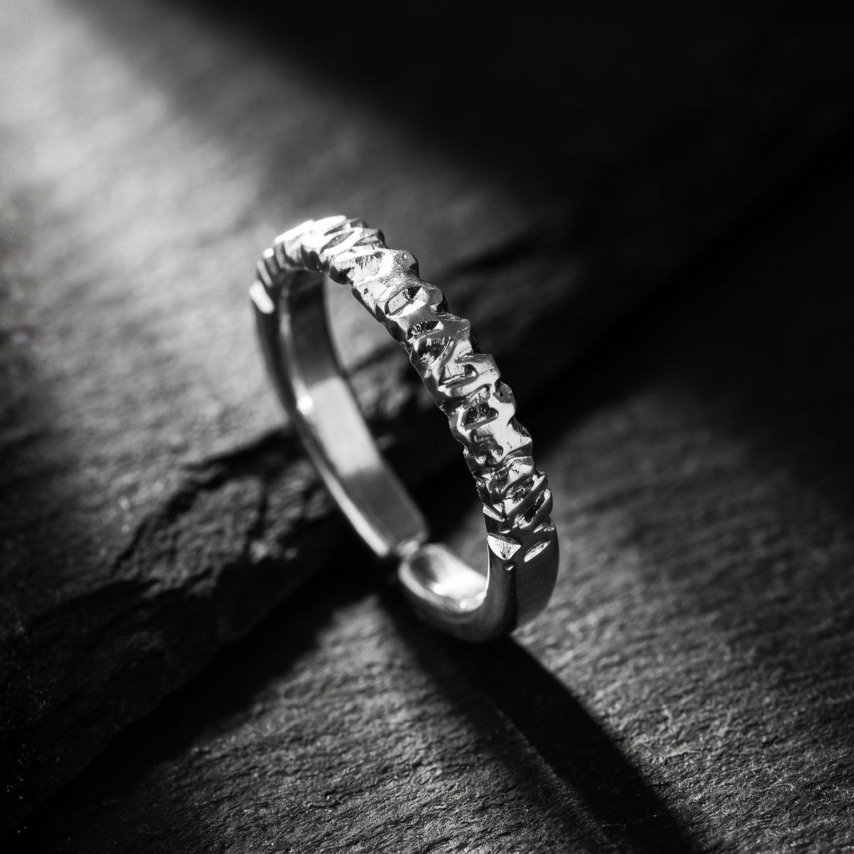 Textured silver open-band ring shown upright at an angle on a rough dark stone surface.